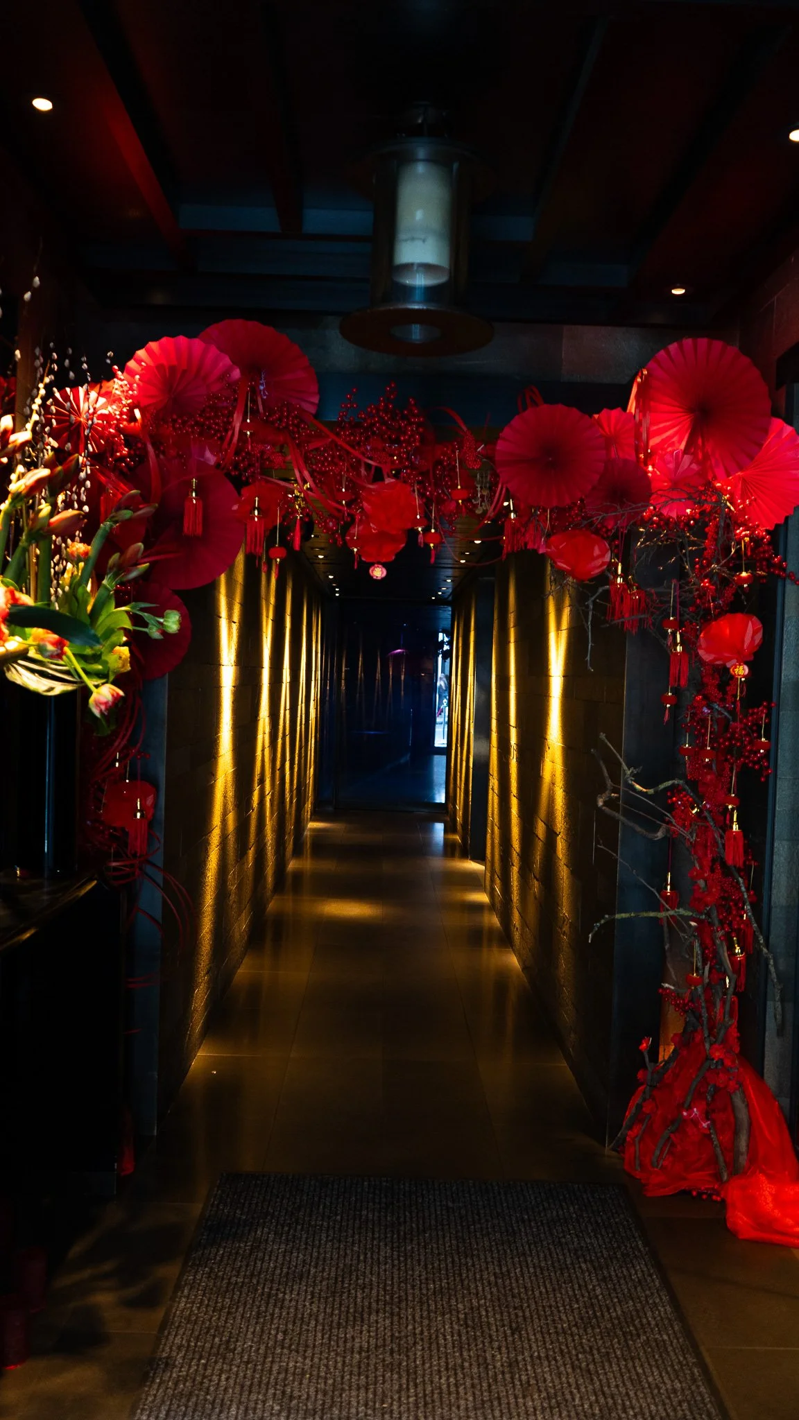 Decorated hallway with red paper fans, red ornaments, and string lights on the ceiling, with gold and black walls and wooden ceiling.