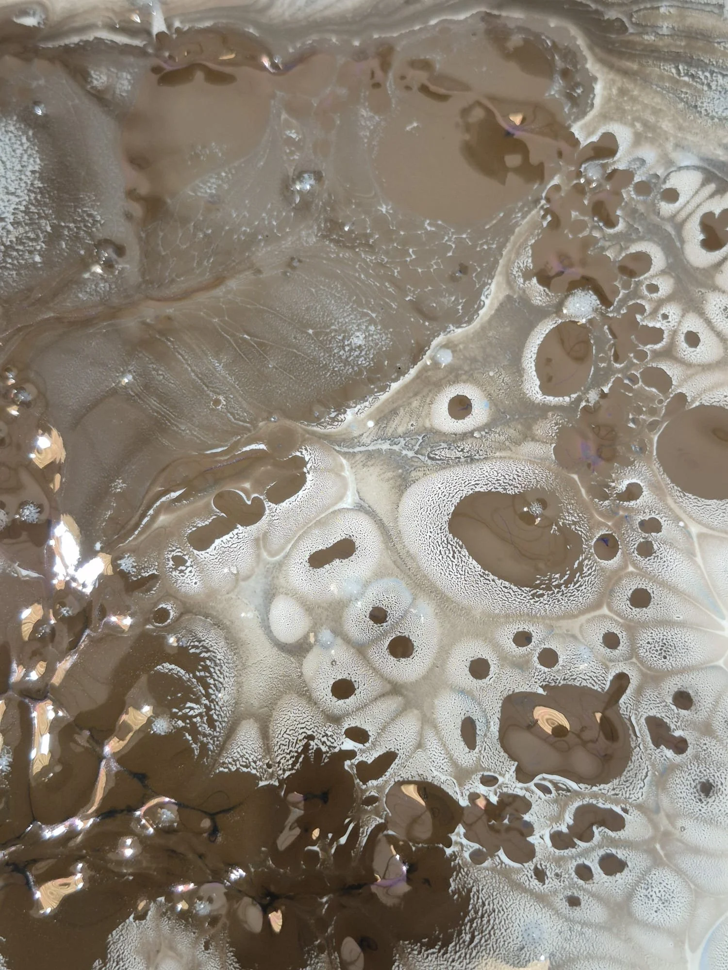 Close-up of a metal surface with numerous circular and irregular holes, some filled with a shiny, reflective material or deposits.