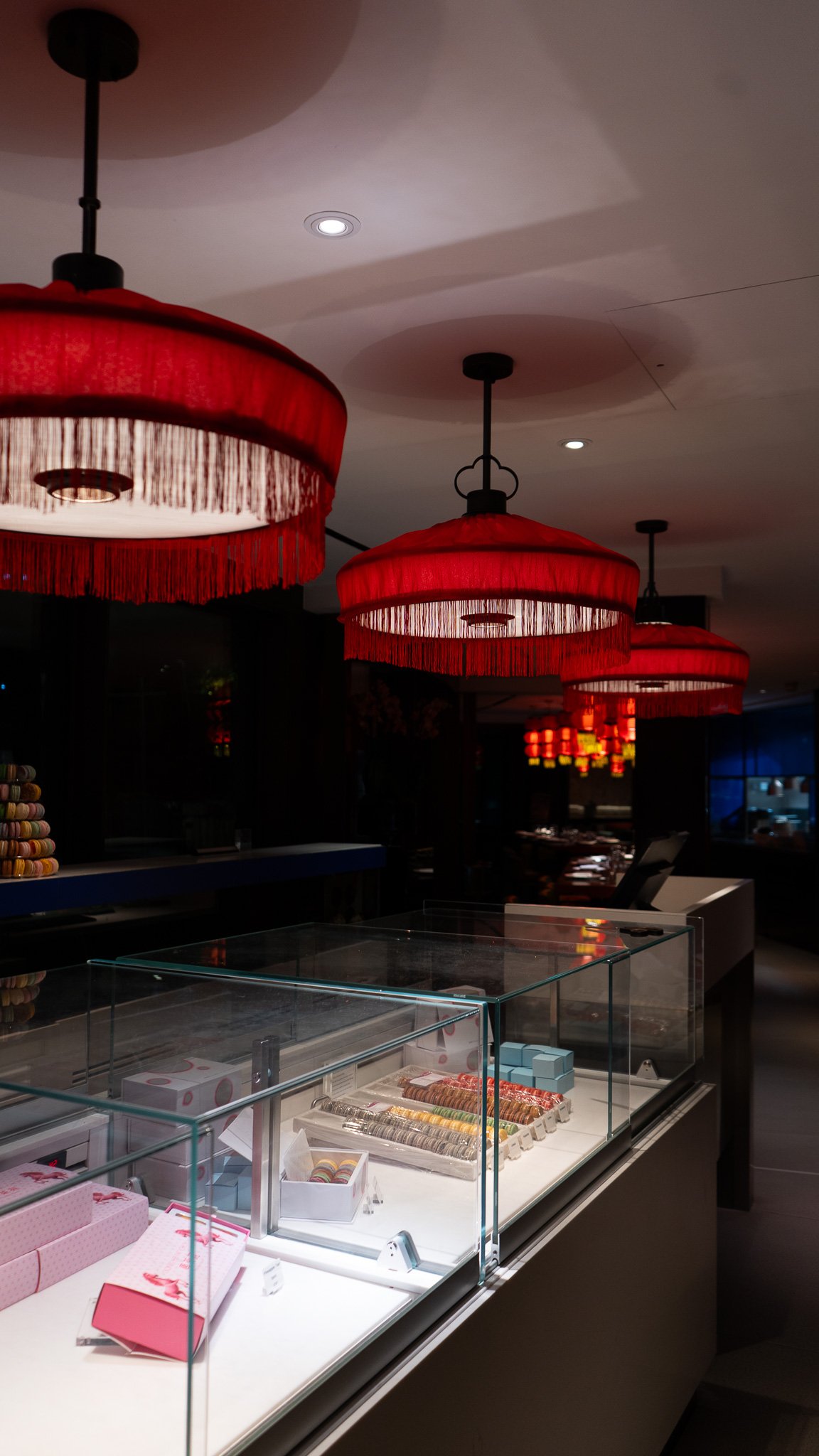 Showcases a display case with Macarons and pink gift boxes in a store, illuminated by red hanging lanterns.