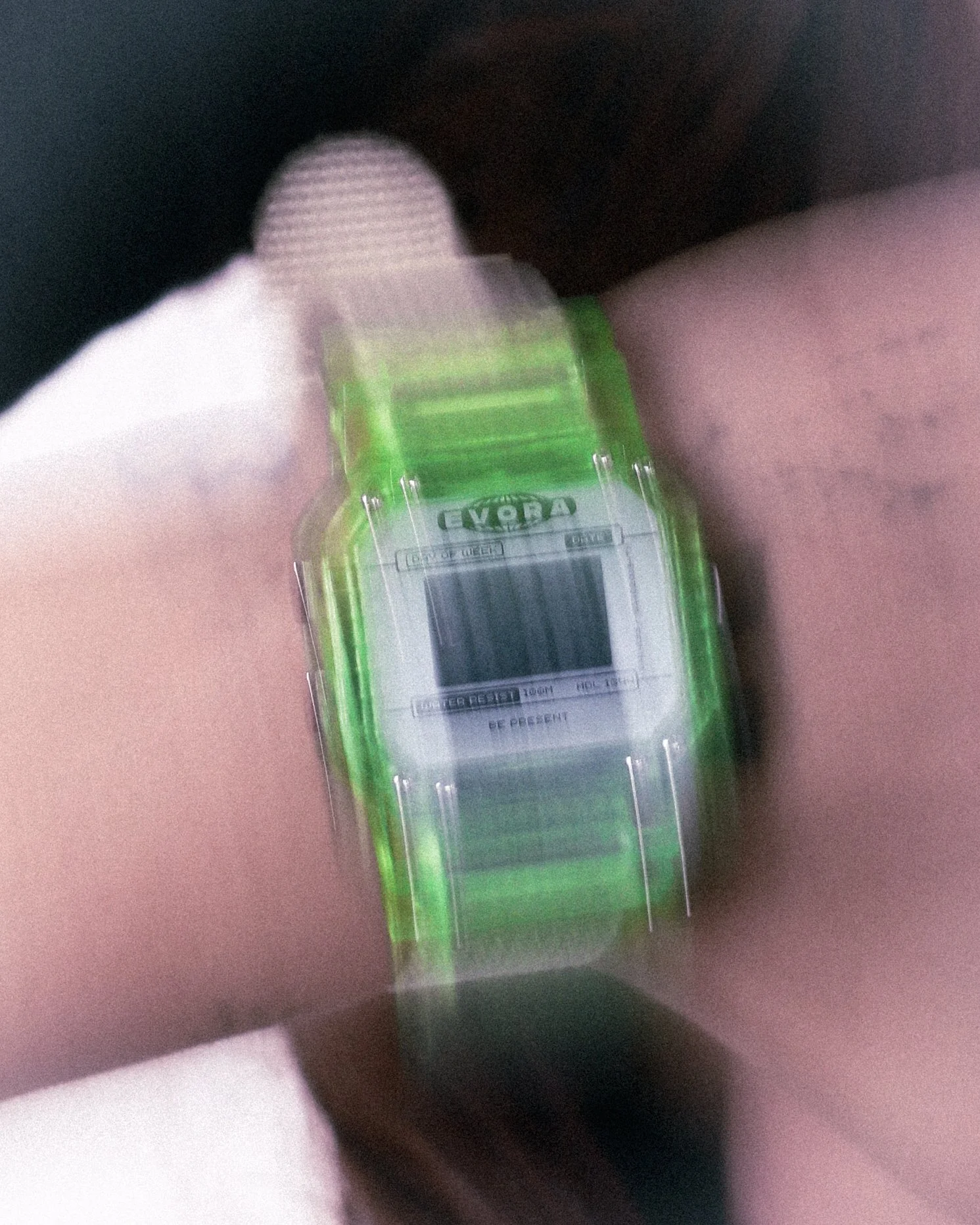A remote control with a green casing, displayed on a pinkish surface with a dark background.