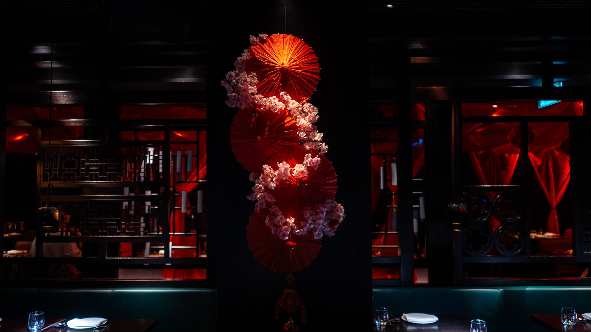Decorative dimly lit restaurant interior with red paper parasols and pink flowers hanging in the center.
