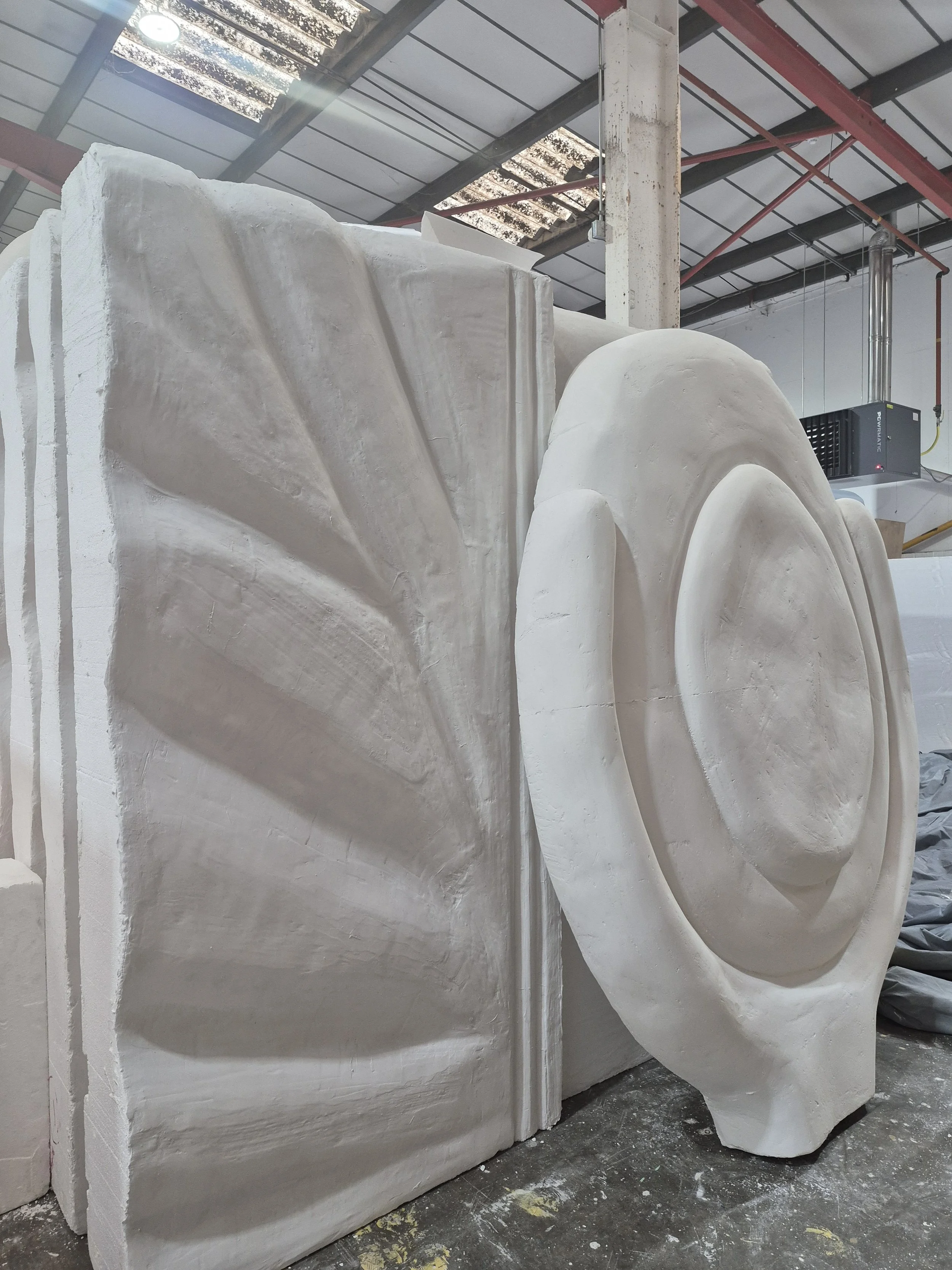 Large white marble sculpture blocks in a workshop with tools and equipment in the background.