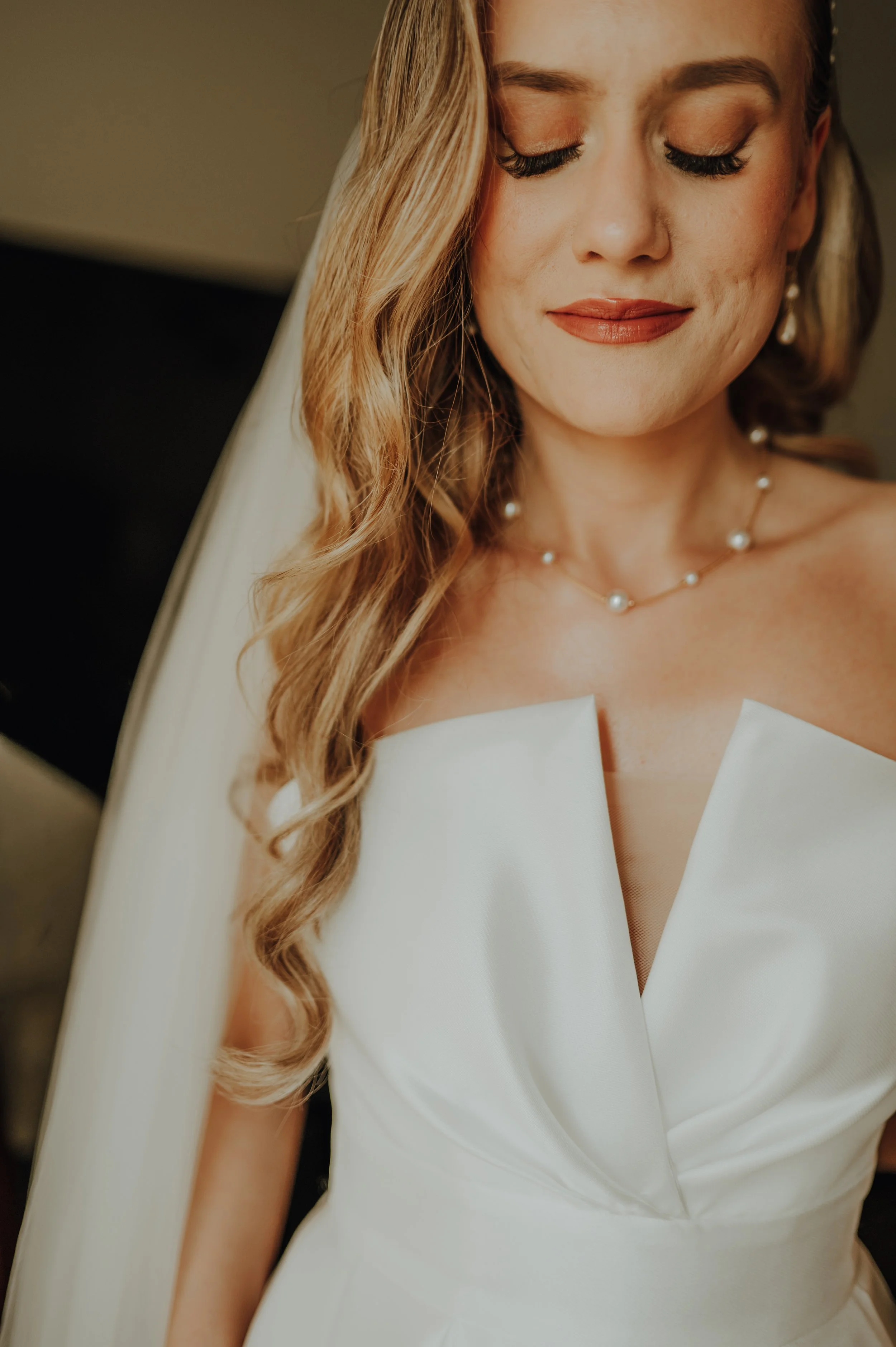 Nahaufnahme eines lachenden Brautpaares, eine Frau mit langen, gewellten blonden Haaren, in einem weißen Kleid mit Perlenkette, geschlossen die Augen, im Hintergrund unscharf.