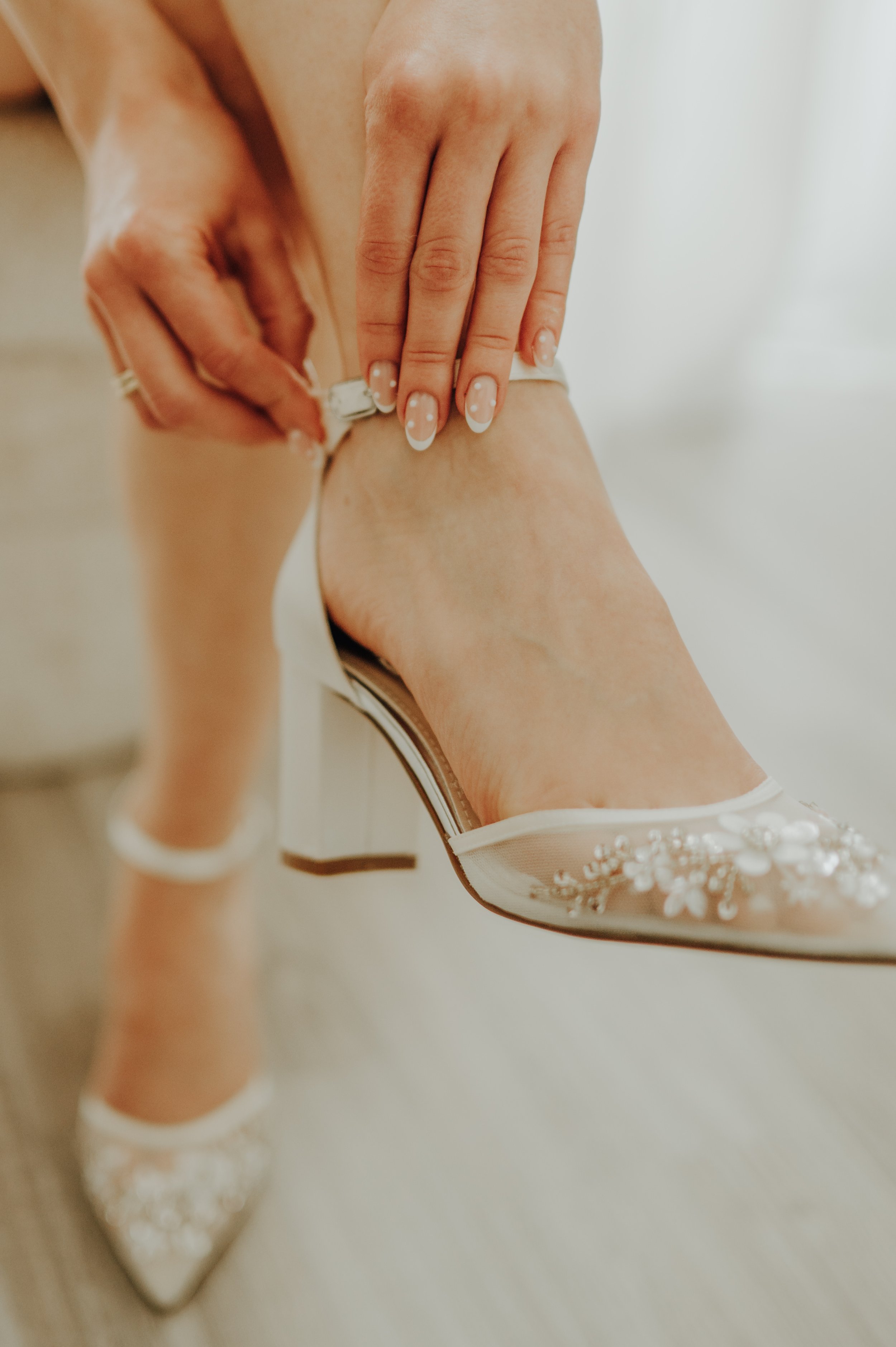 Nahaufnahme einer Frau, die weiße High Heels mit Perlen verziert anzieht.