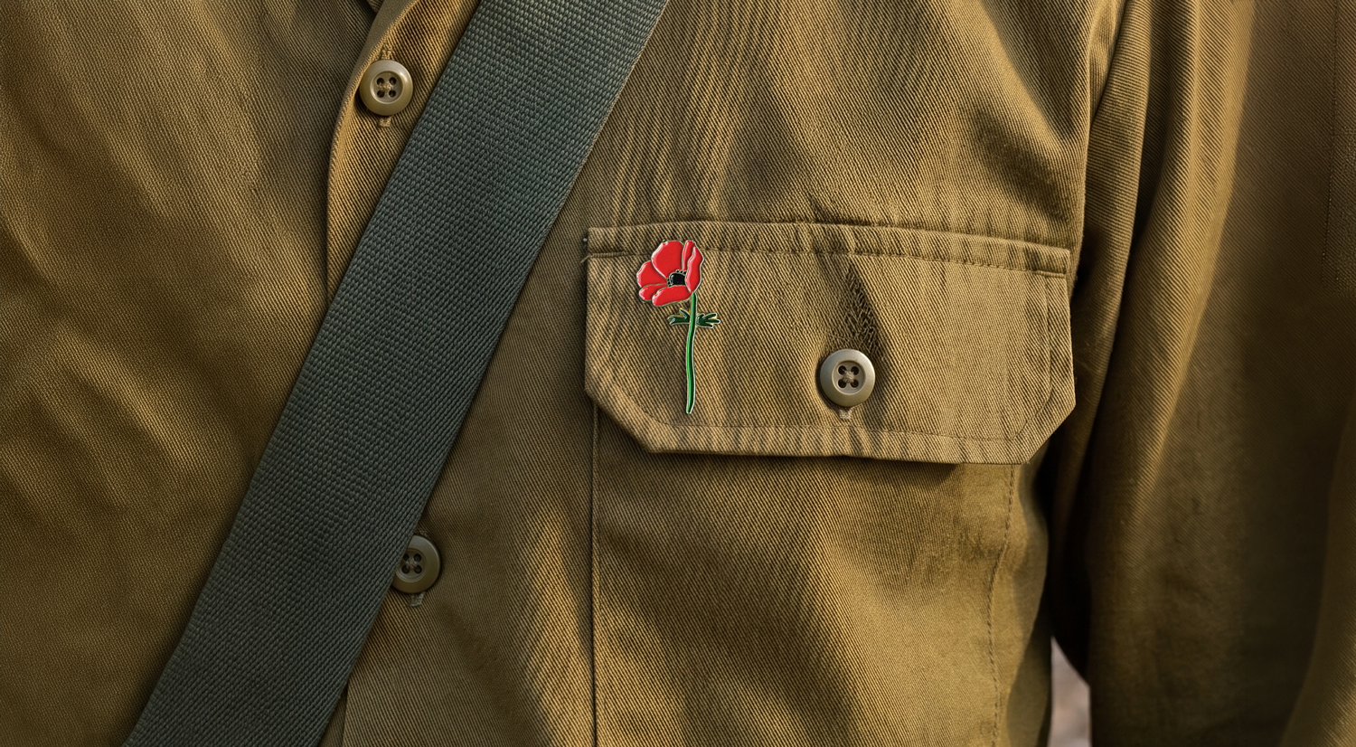 Close-up of a person in a khaki IDF uniform with a Crown Anemone pin on the pocket and a green strap across the chest.