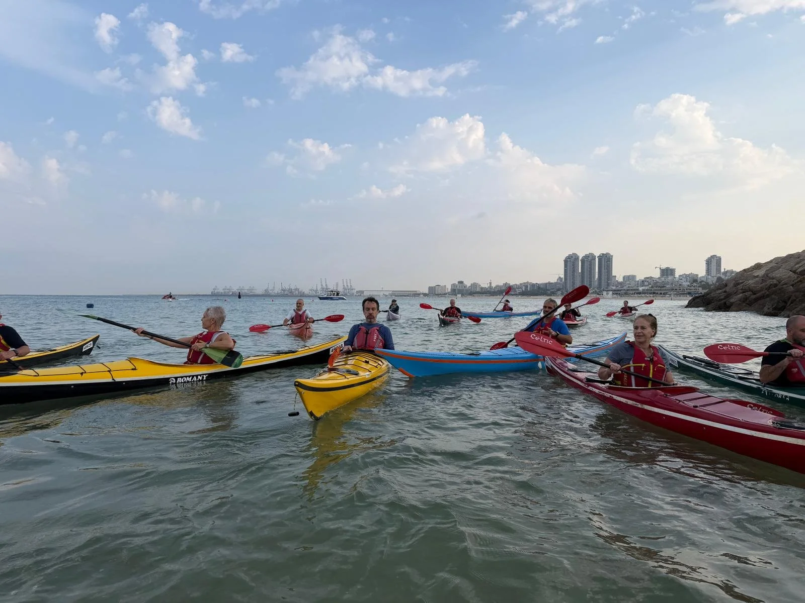 People kayaking in a harbor with city buildings in the background on a clear day.