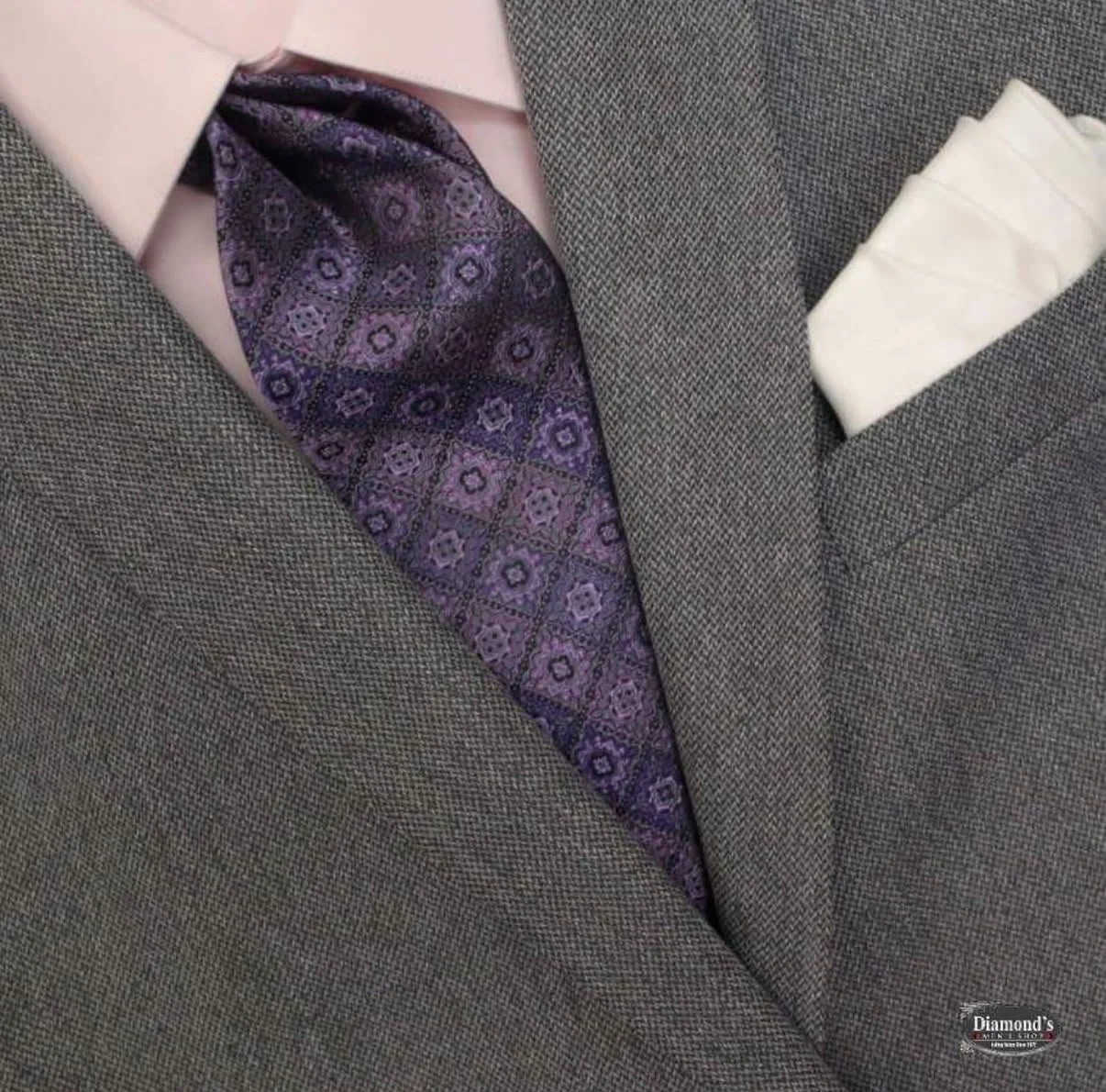 Close-up of a men's suit jacket with a purple patterned tie, a pink dress shirt, and a white pocket square.