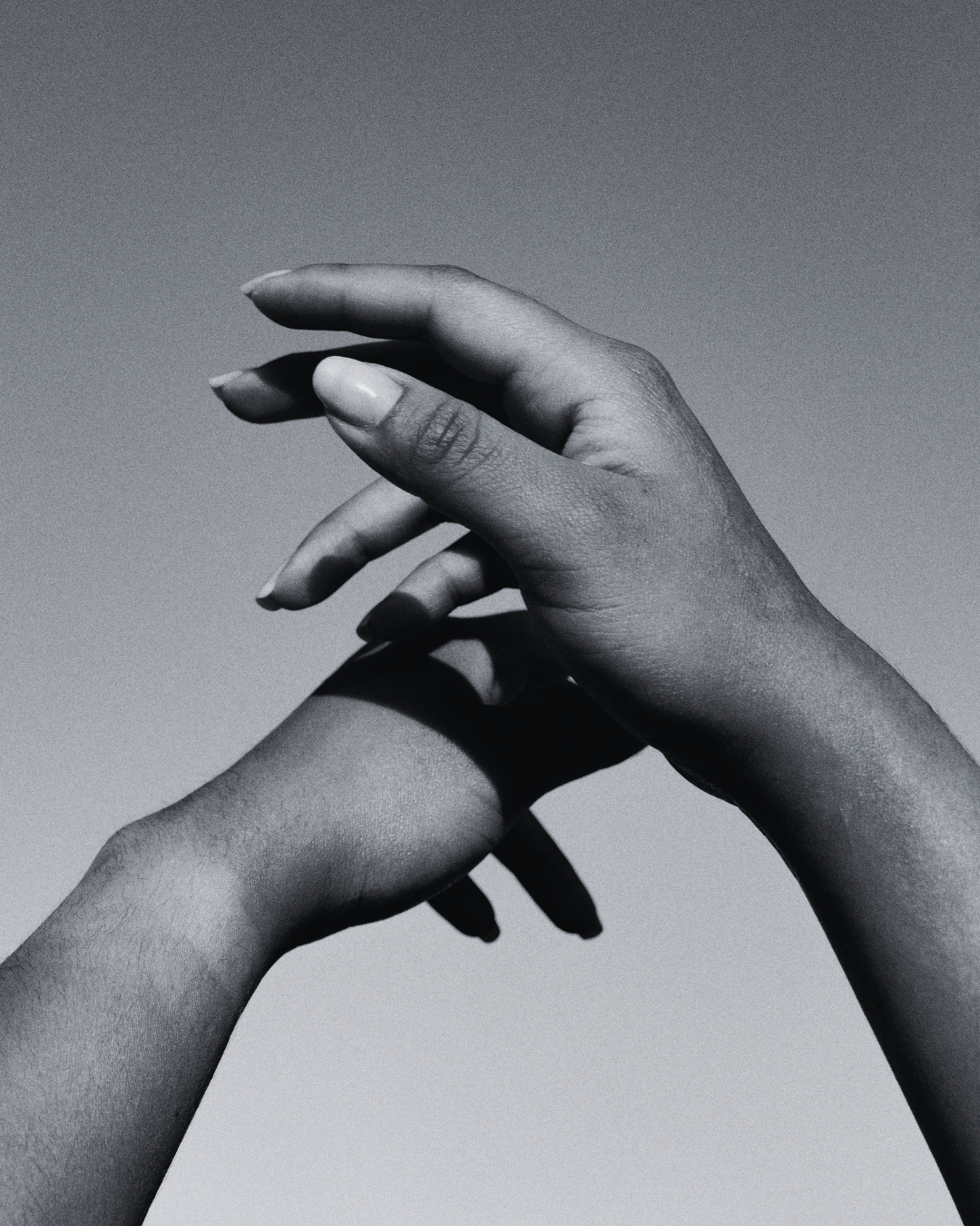 Two hands interlaced, one gently resting on top of the other, against a plain background.