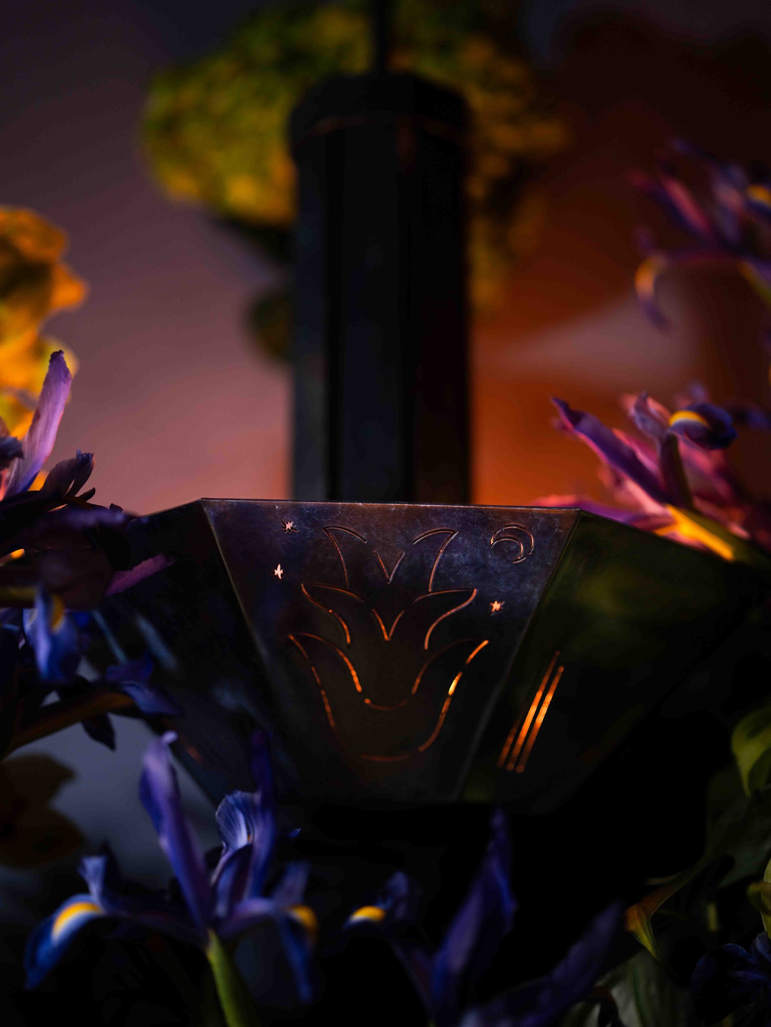 A lit lantern surrounded by flowers at night.