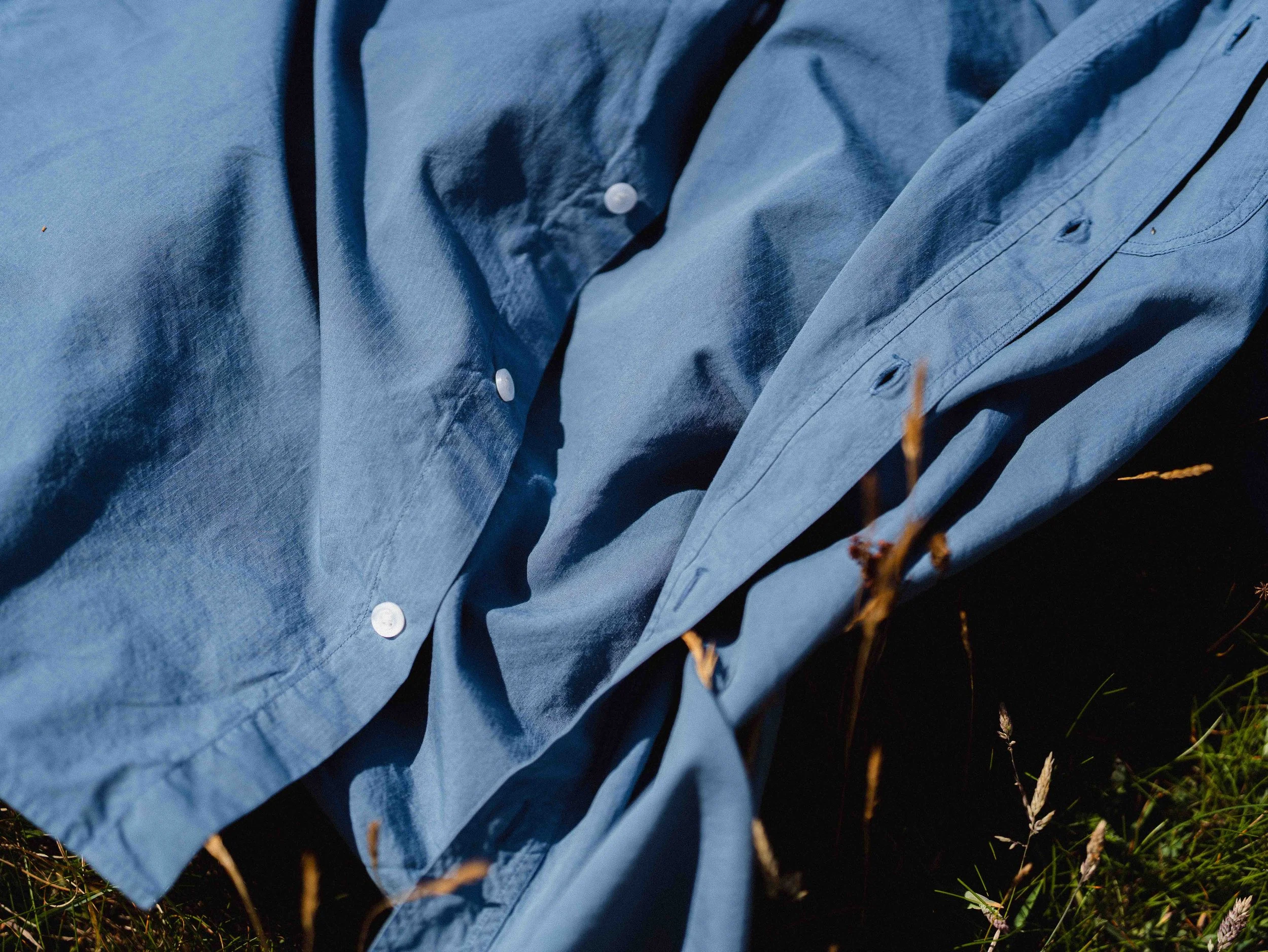 Blue long-sleeve button-up shirt laying on the grass in a nighttime outdoor setting.