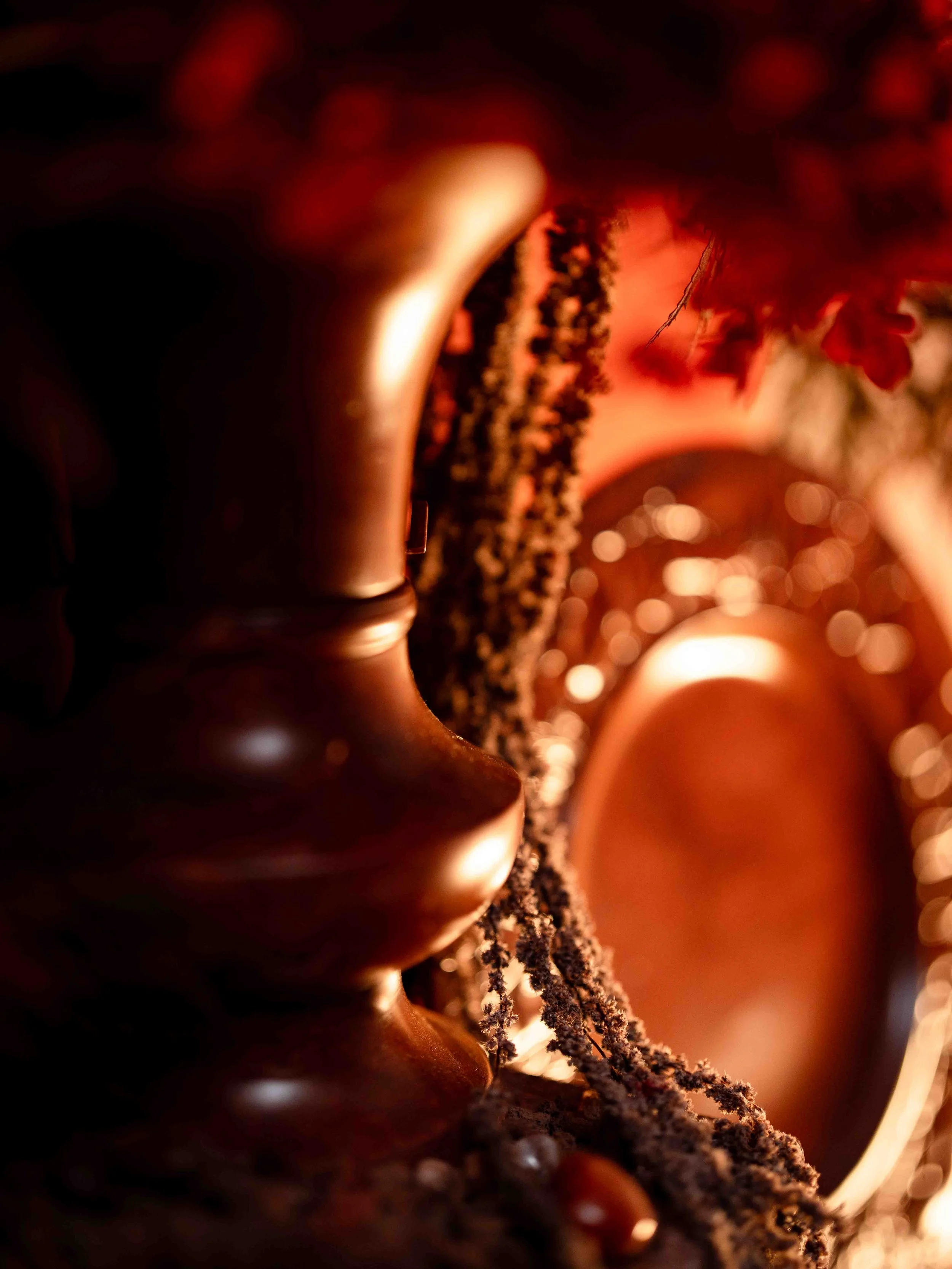 Close-up of a person's neck and shoulder, with curly hair and a hint of a face, illuminated by warm, reddish lighting.