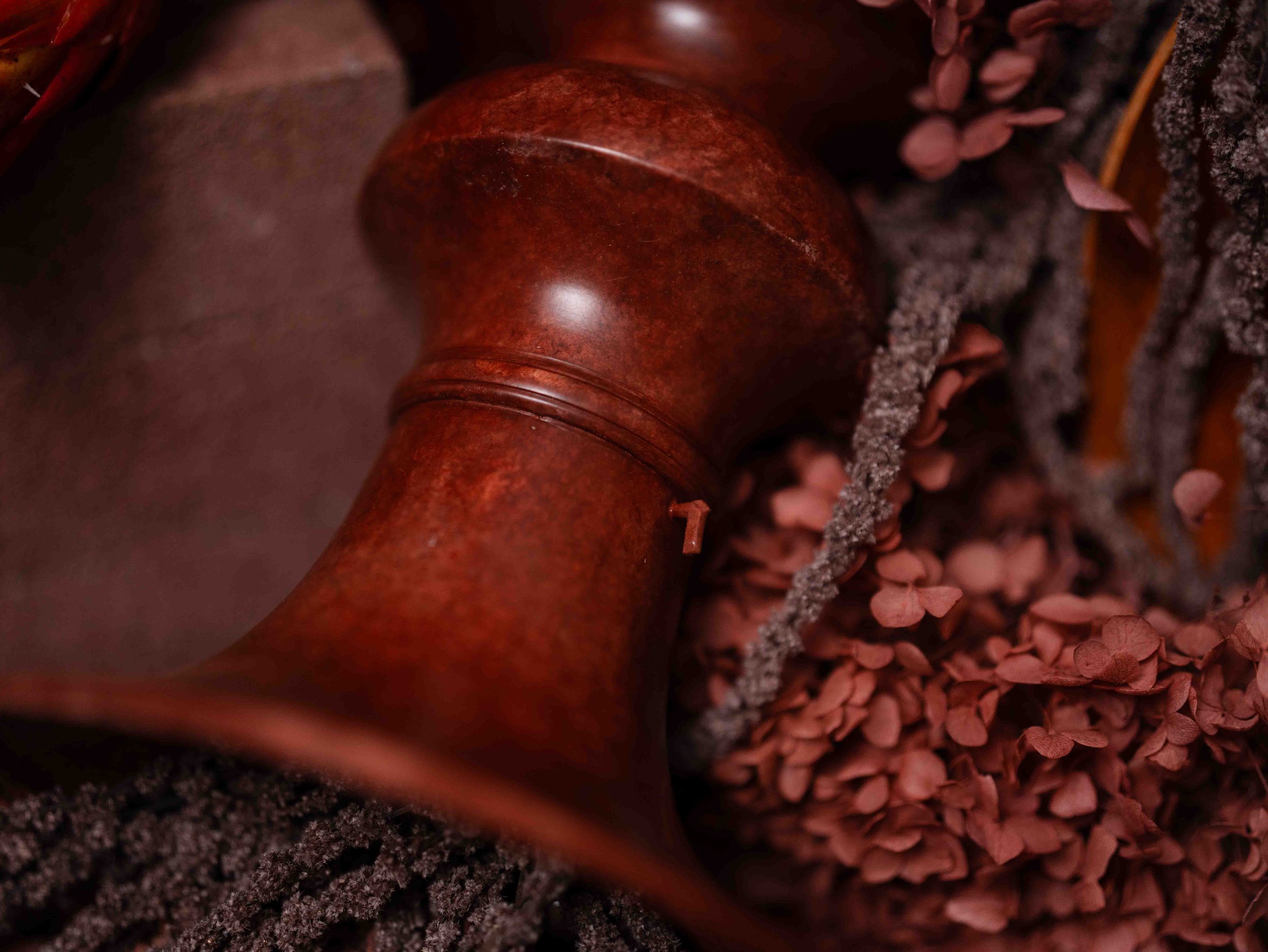 Close-up view of a crafting or grooming tool, possibly a wooden handle, resting on a surface of small, reddish granules or pellets, with some sparkling or textured elements nearby.