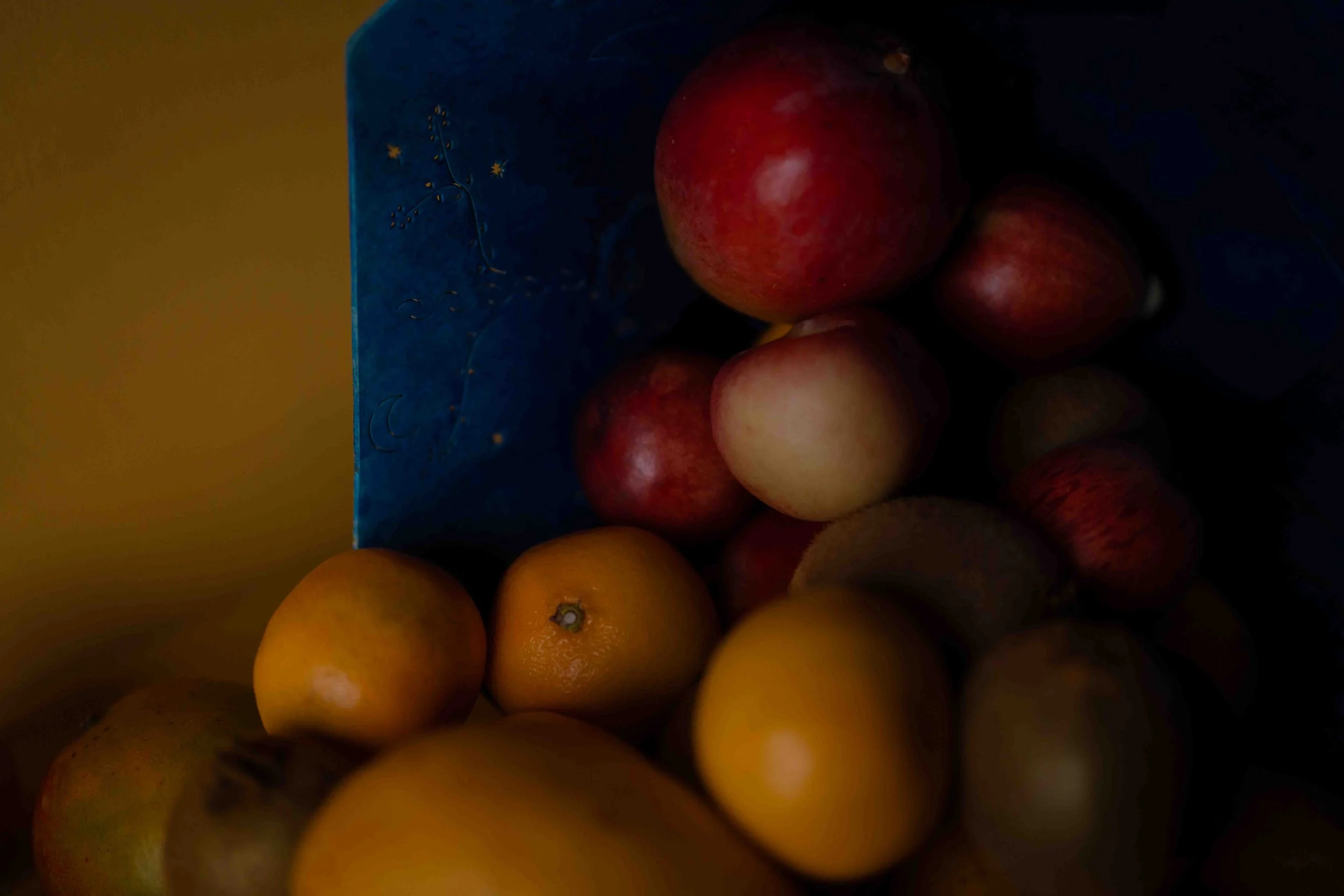 A collection of apples and oranges in a dark setting, with a blue box partially visible.