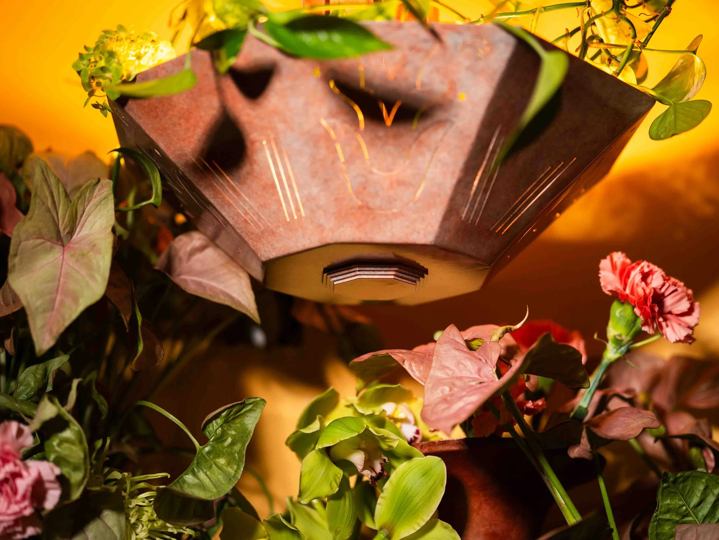 Close-up of a decorative lantern surrounded by pink, green, and red leaves, with a yellow background.