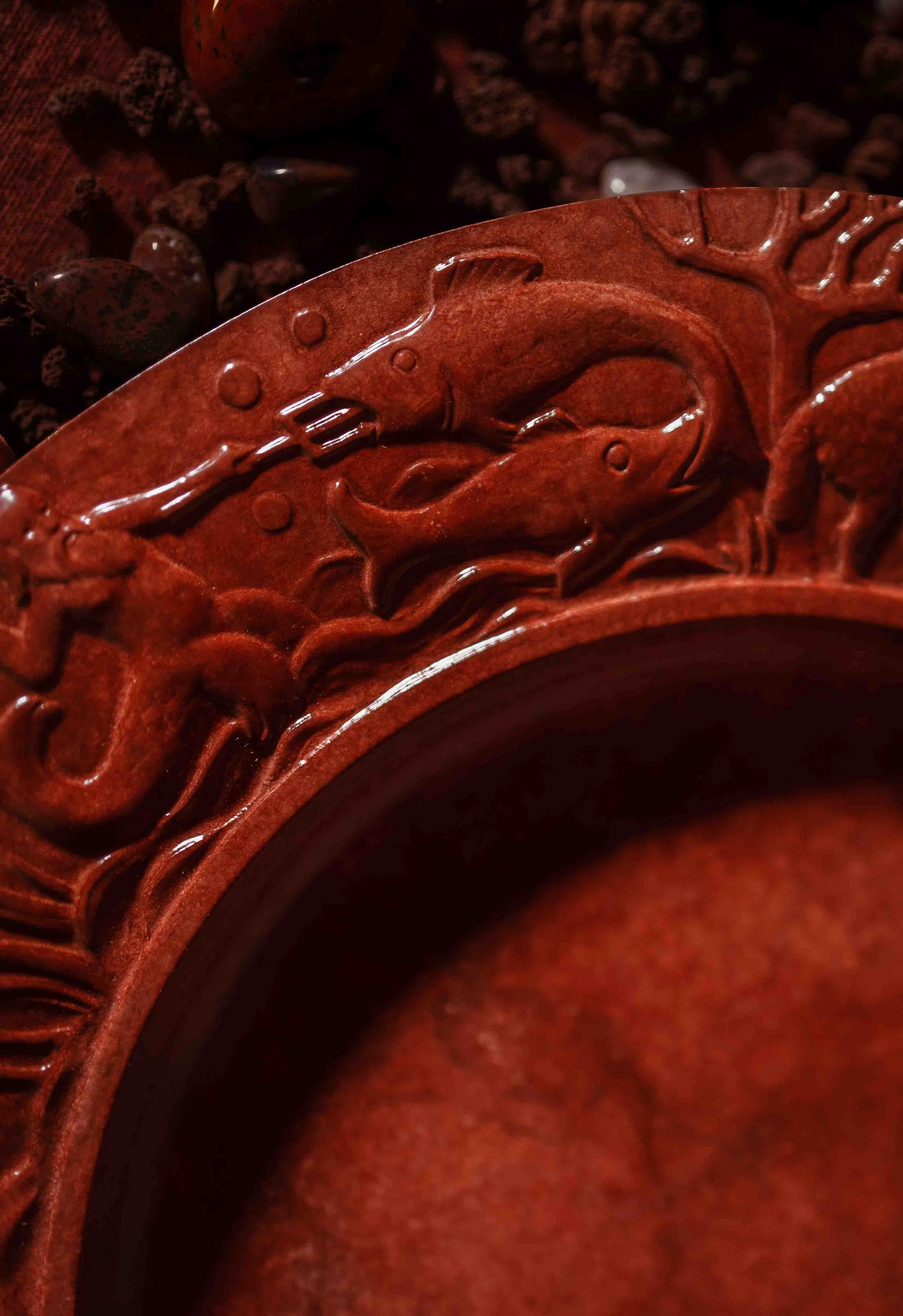 Close-up image of a carved wooden object with intricate fish designs, reddish-brown color, and shiny finish.