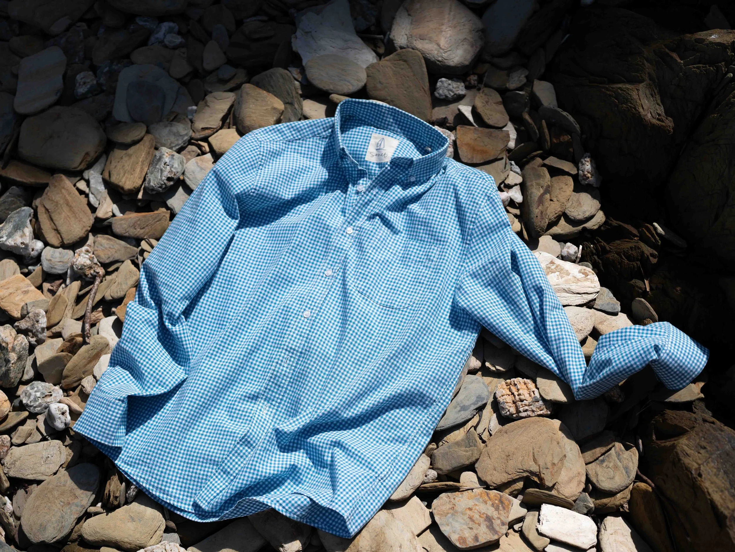 A blue checkered long-sleeve shirt lying on a bed of rocks and stones outdoors.