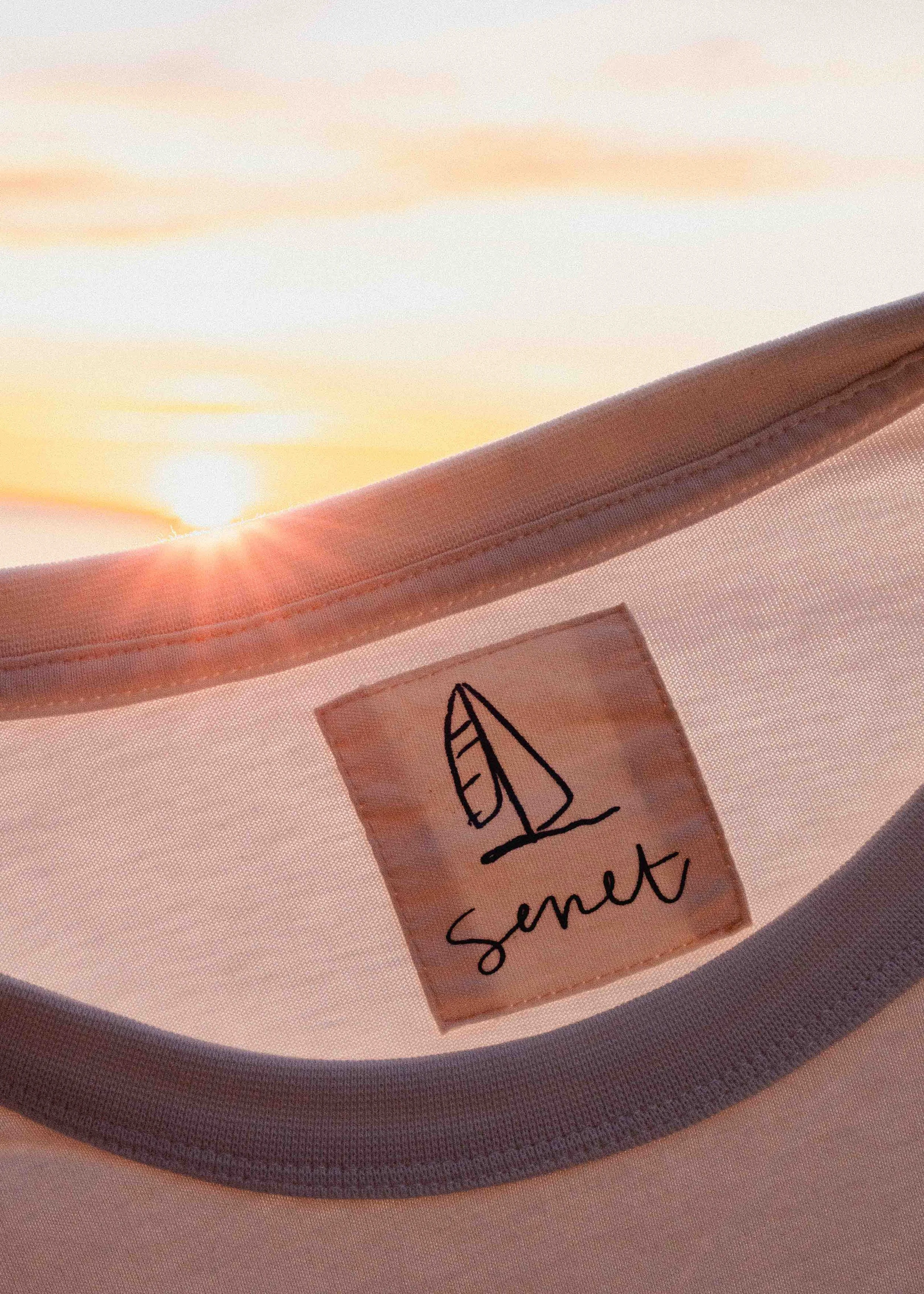 Close-up of a fabric label with a leaf logo and the word 'sent' underneath, against a background of soft sunlight and fabric.