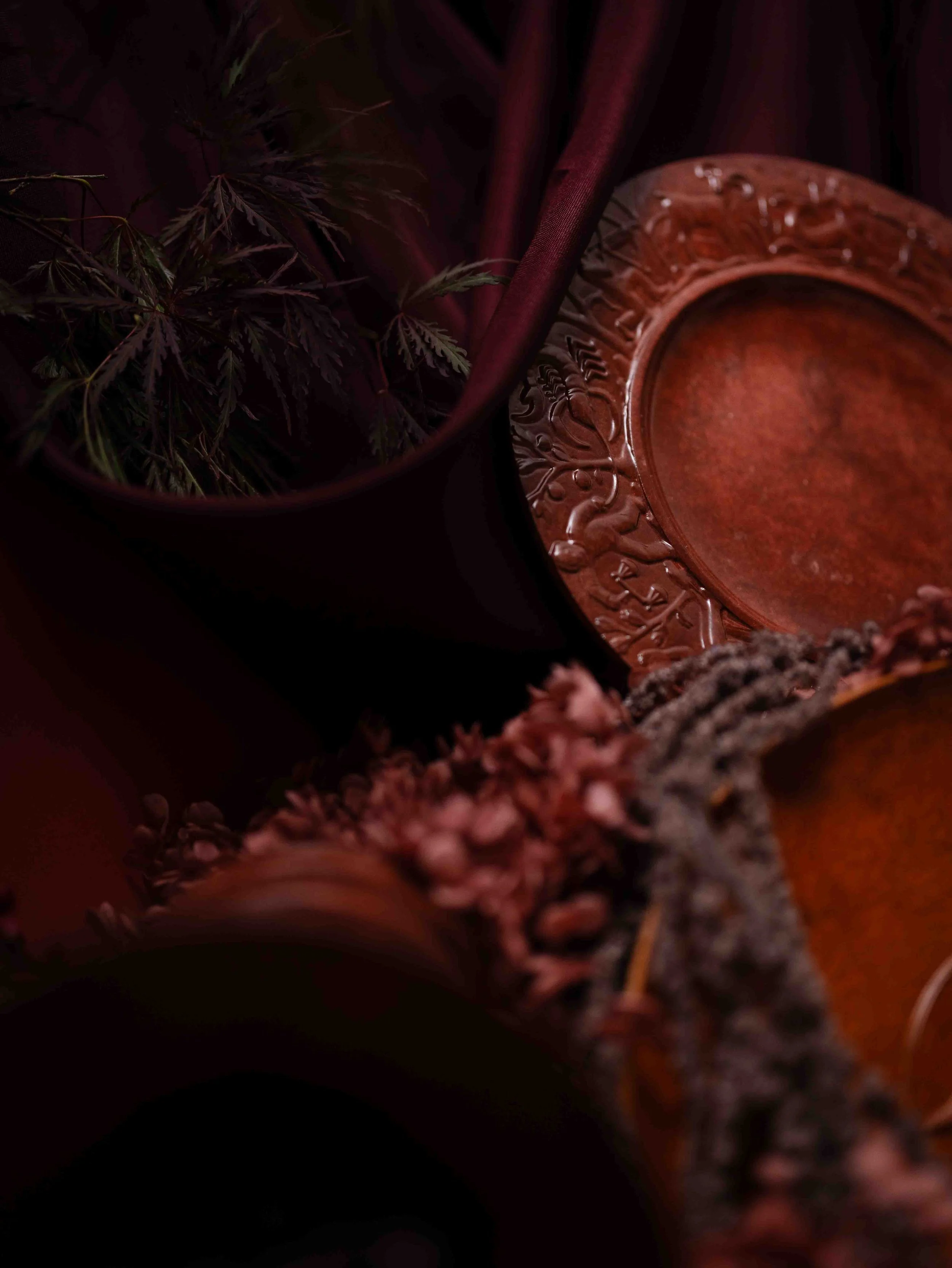 Close-up of a dark-colored pot with green foliage inside, beside a decorative reddish-brown ceramic dish with patterns.