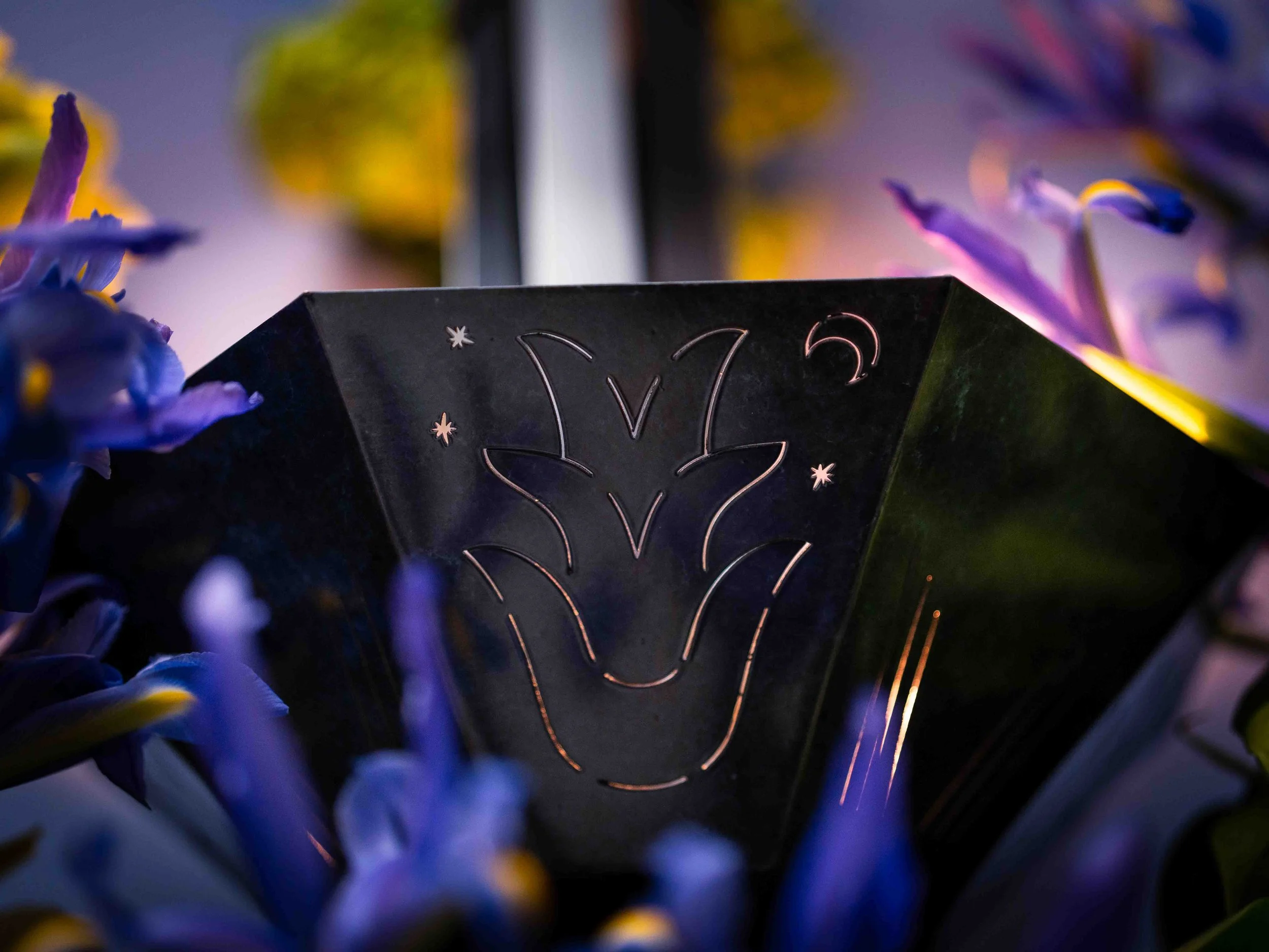 Close-up of a black object with a design of a smiling face and stars, surrounded by blurred purple and yellow flowers in the background.