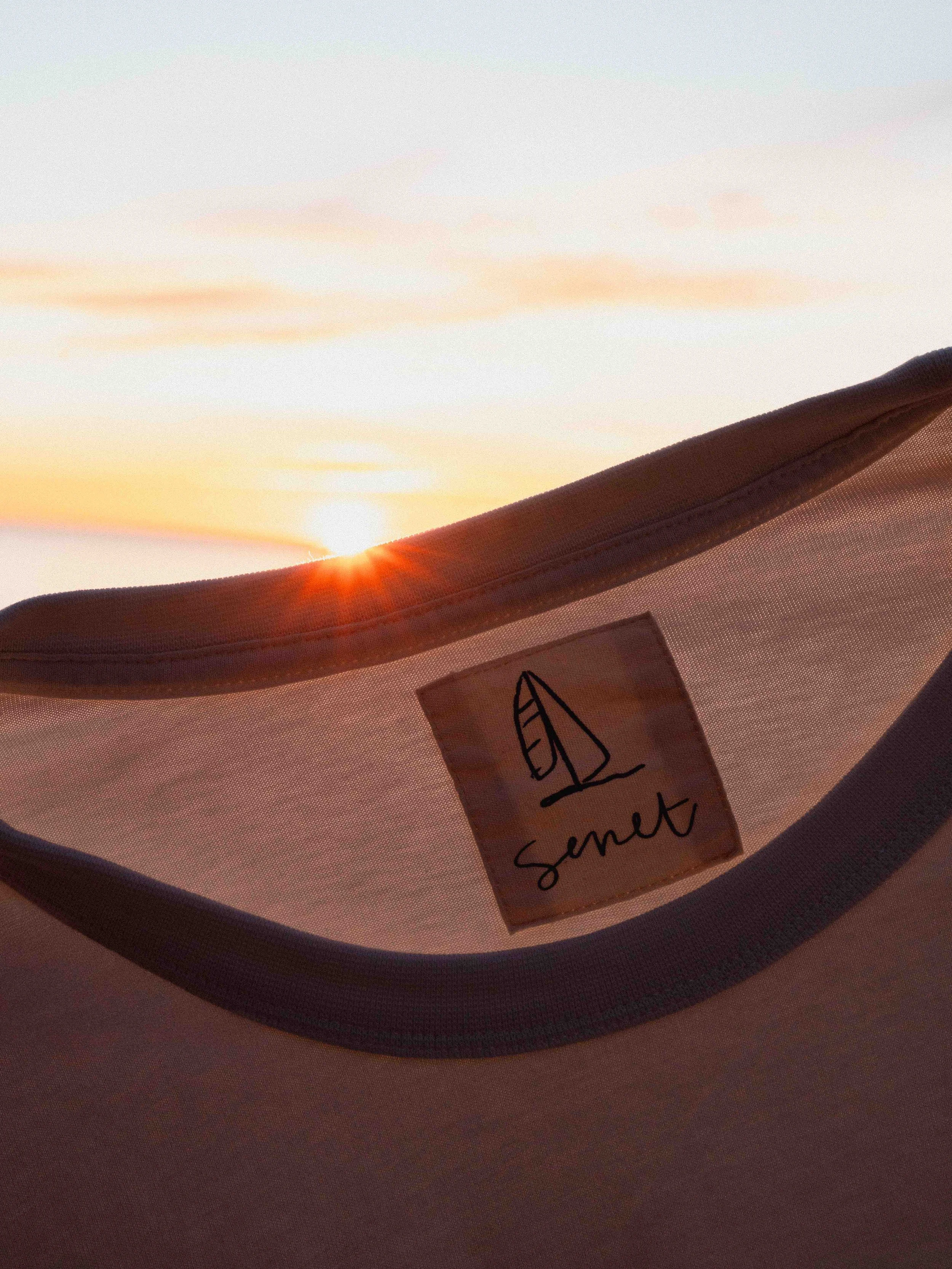 Sunset over the ocean with a small sailboat, and a fabric tag with the words "Sand" attached to a surface.