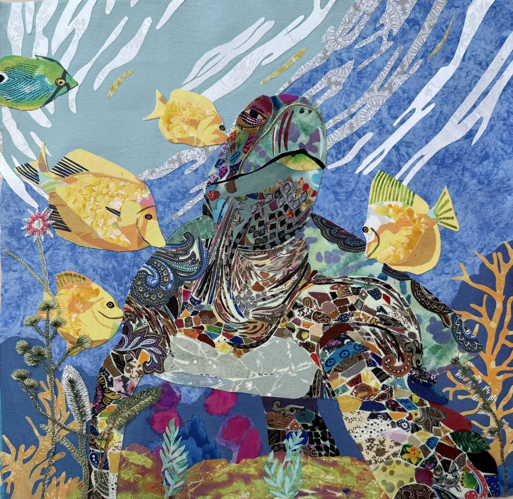 Colorful collage artwork featuring fish, a butterfly, and abstract patterns on a blue background, with green foliage accents.