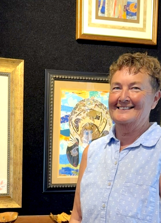 A woman smiling in front of colorful framed artwork at an art gallery.