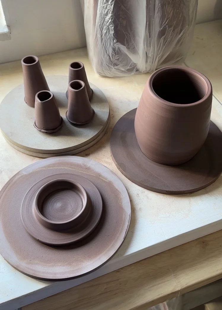 Unfired clay teapot items on a worktable.