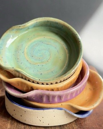 Stacked colorful ceramic spoon rests on a wooden surface.