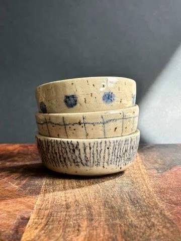Three stacked ceramic bowls with various patterns on a wooden surface against a dark background