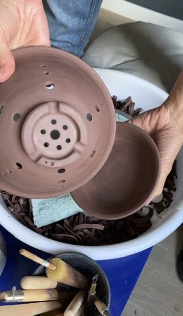 A berry bowl with a water container over a splash pan filled with trimmed clay and tools.