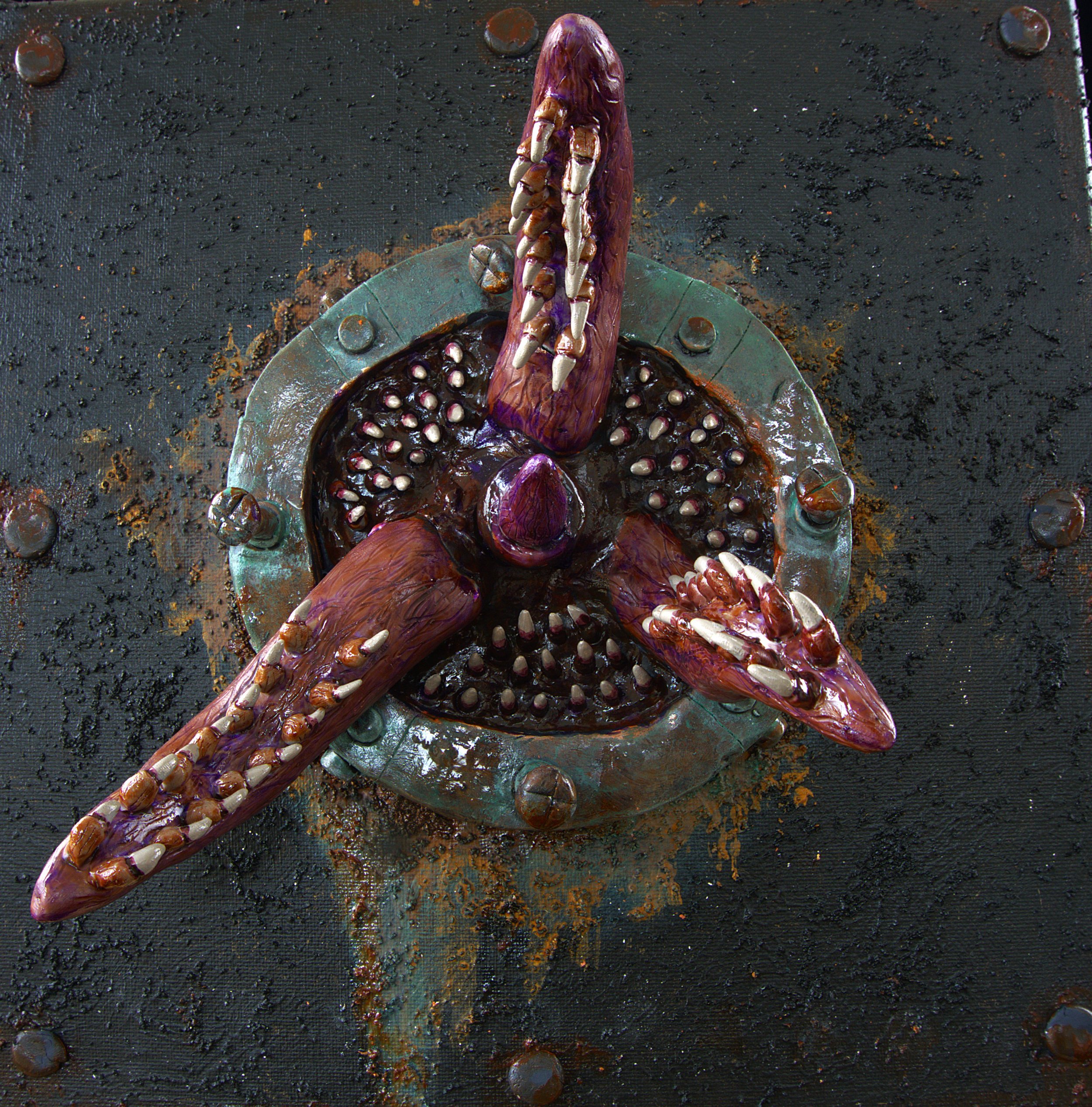 Close-up of a sculpture of a purple and brown snake with large fangs, coiled in a bowl filled with round, shiny objects, on a textured black surface with scattered bumps and a few metallic elements.