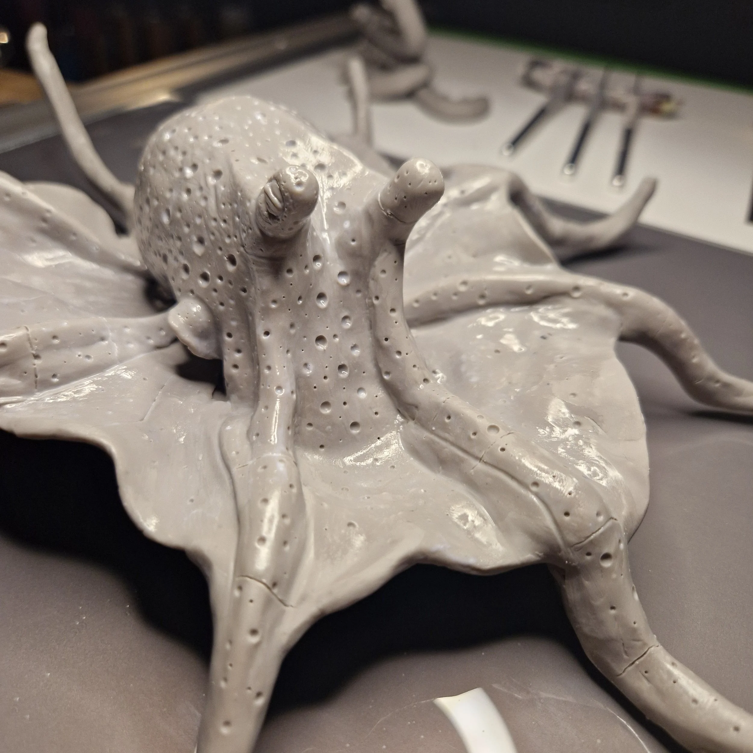 Close-up of a melted and dripped white plastic object with a bumpy surface, placed on a gray surface with various metal tools in the background.