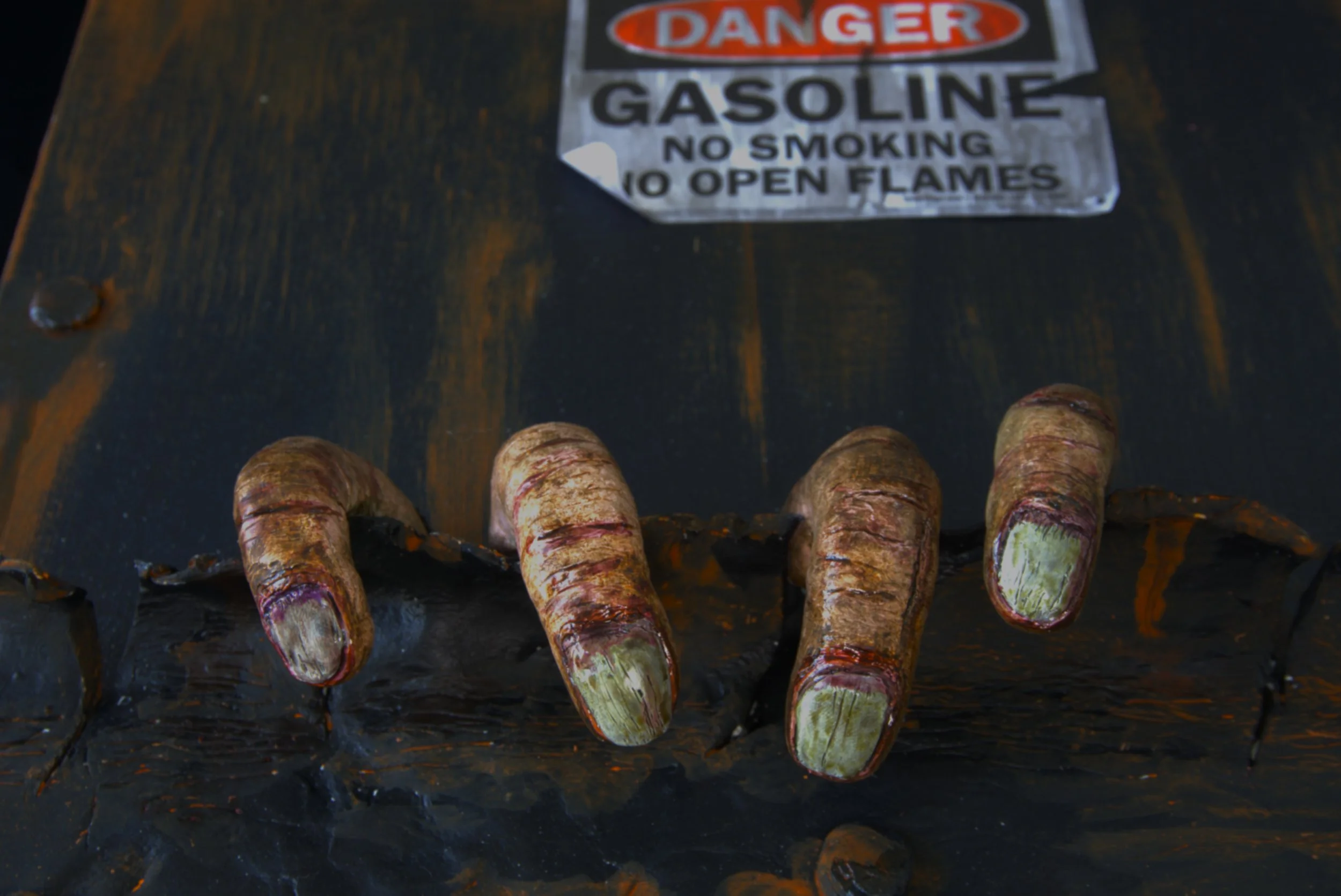 Close-up of a row of burnt fingers in front of a danger sign on a dark wooden surface.