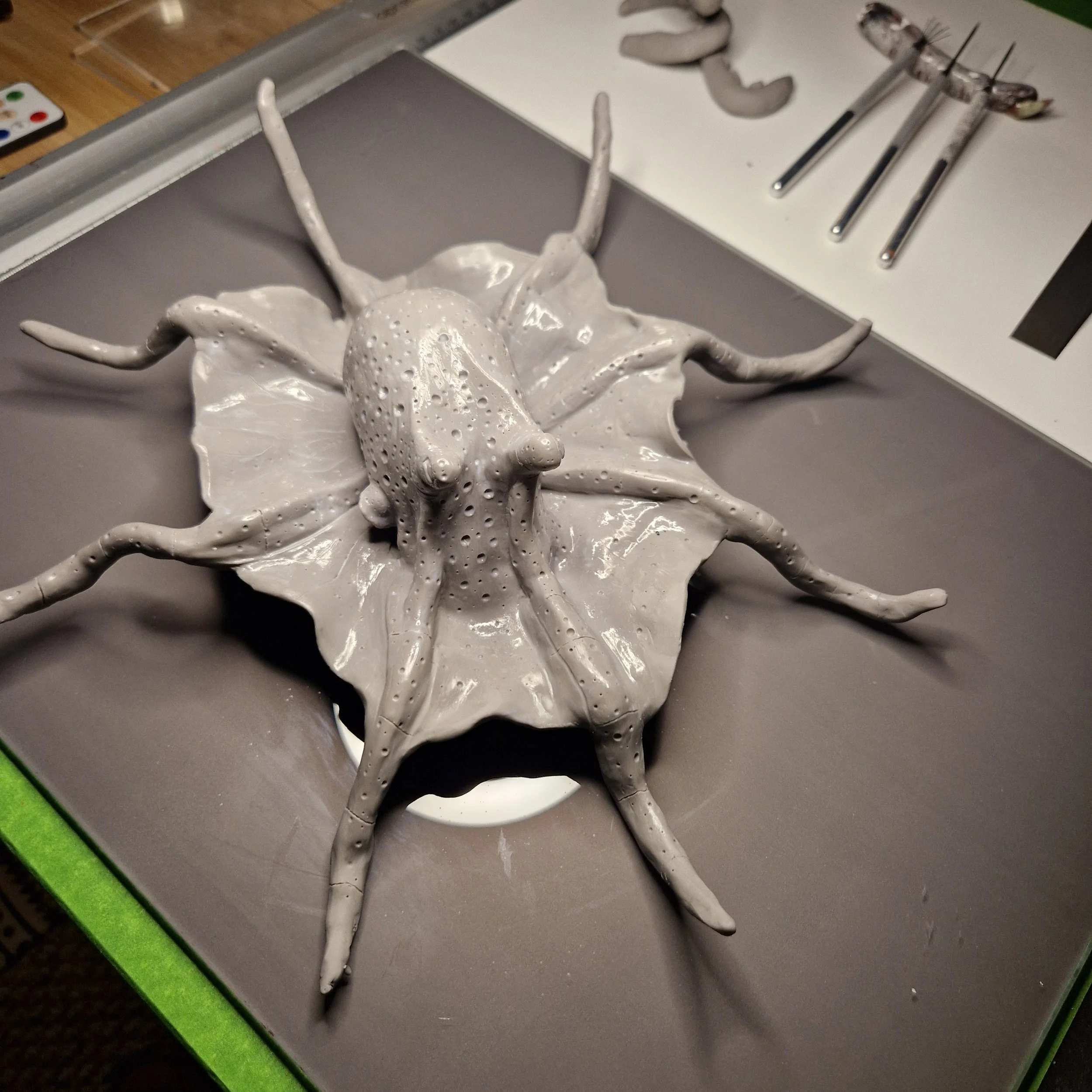 A white ceramic sculpture of an octopus on a gray table, with paintbrushes and a white palette nearby.