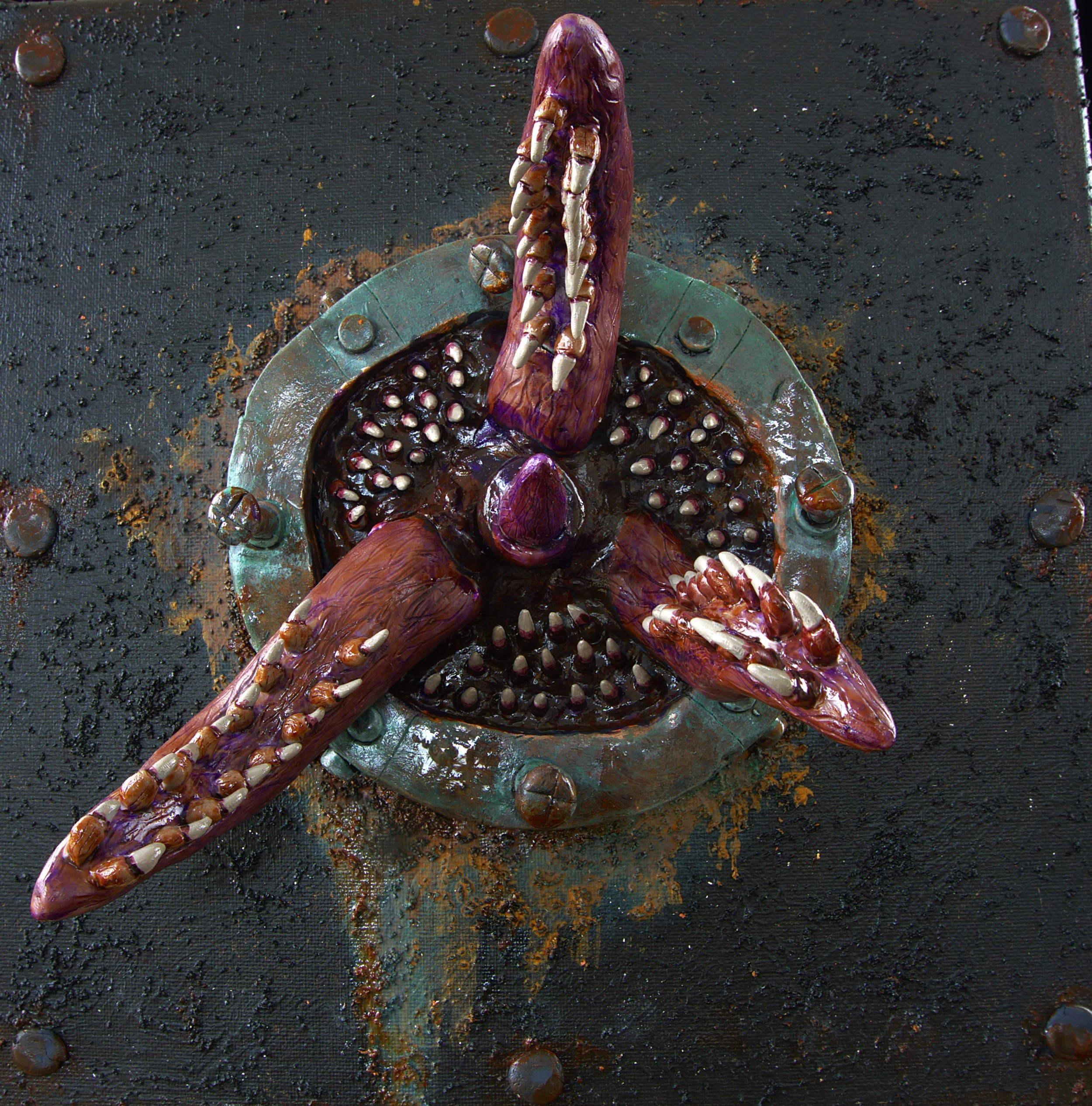 A sculpture resembling a distorted, elongated creature with multiple claws or tentacles, painted in shades of purple and brown, set on a textured black background with scattered metallic elements.
