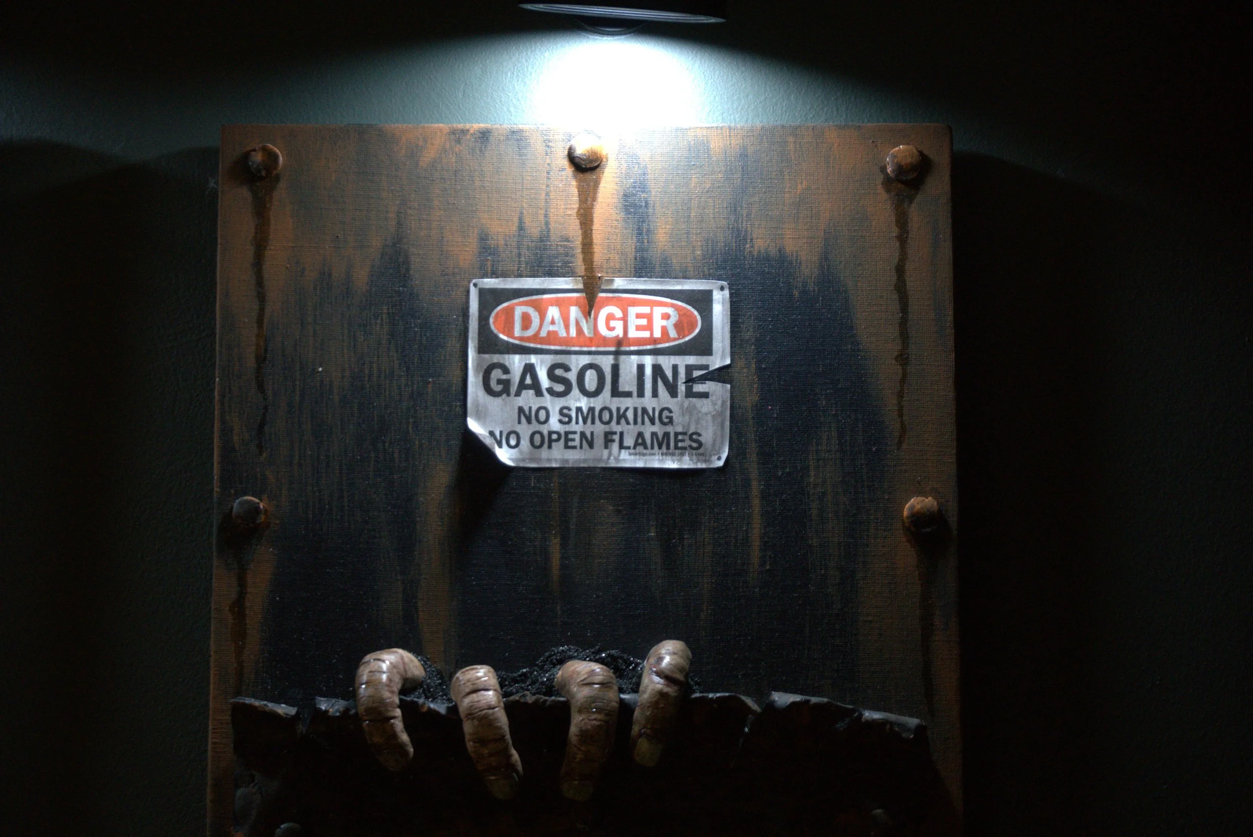 A wooden wall with a metal danger sign that says 'DANGER GASOLINE NO SMOKING NO OPEN FLAMES' and a row of caterpillars at the bottom.