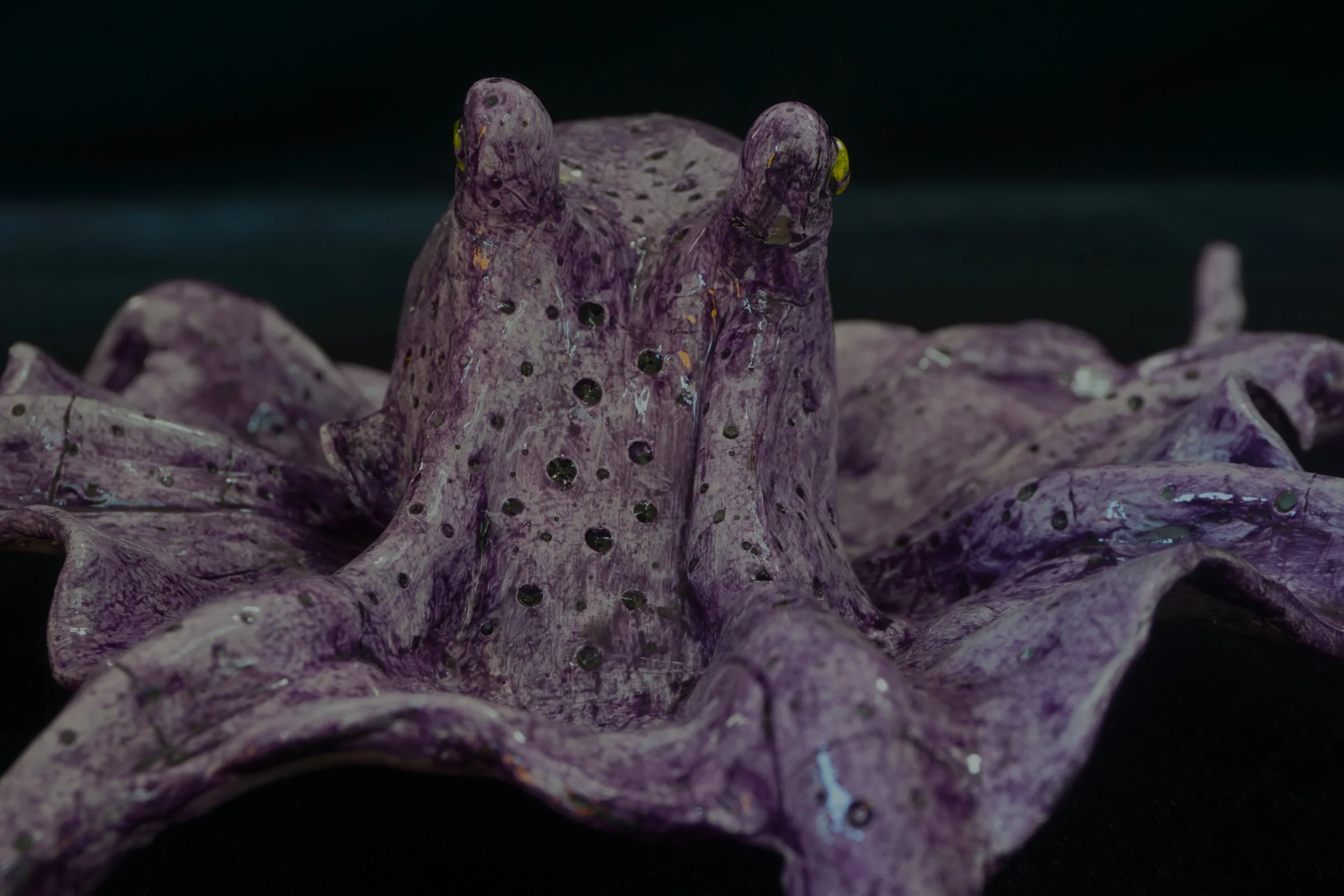 Close-up of a purple and black marbled ceramic sculpture with a textured surface, resembling a stylized animal or creature, with a dark background.