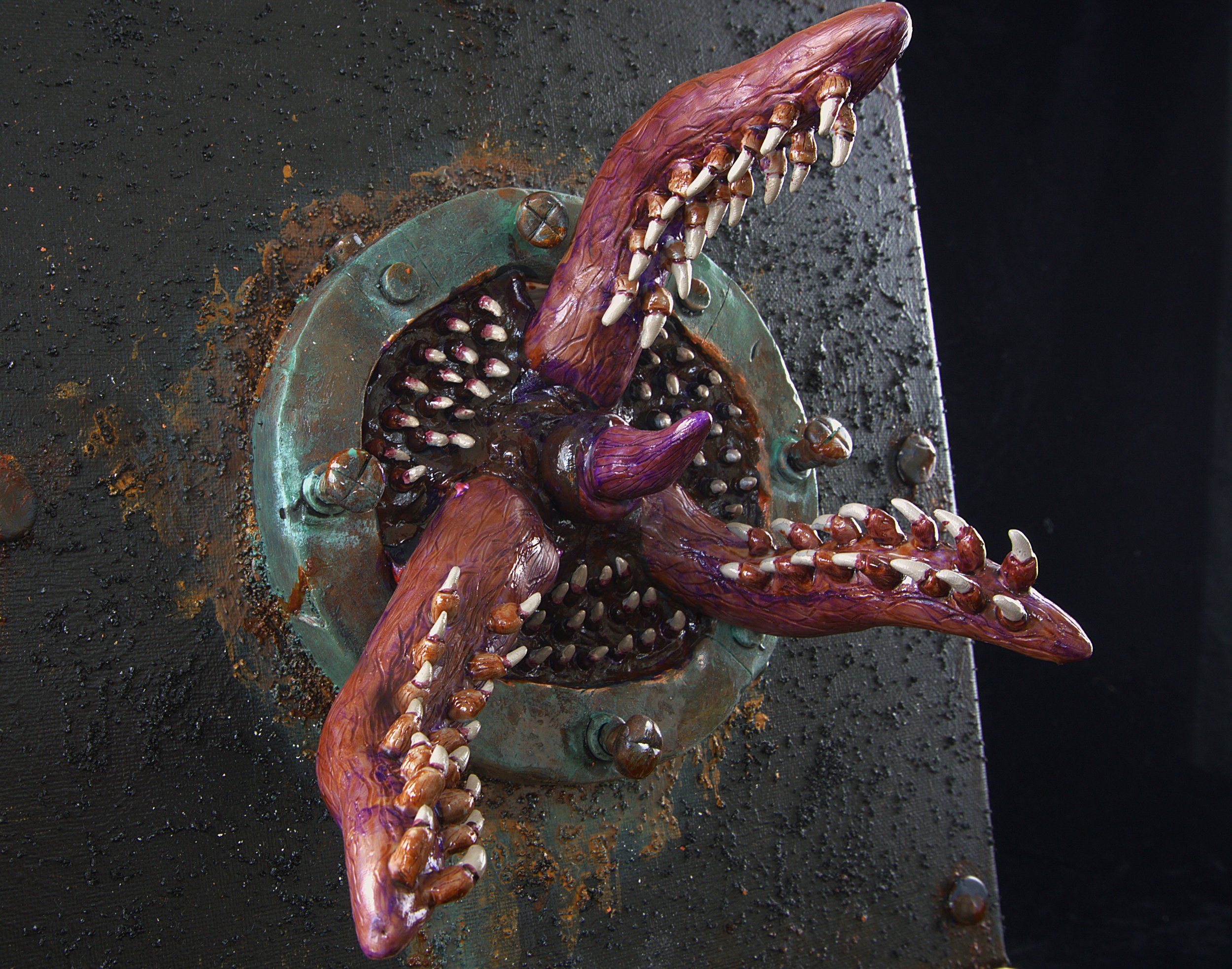 A sculpture resembling a creature with a large, elongated mouth filled with sharp teeth, mounted on a metallic base with bolts, surrounded by rust and debris.