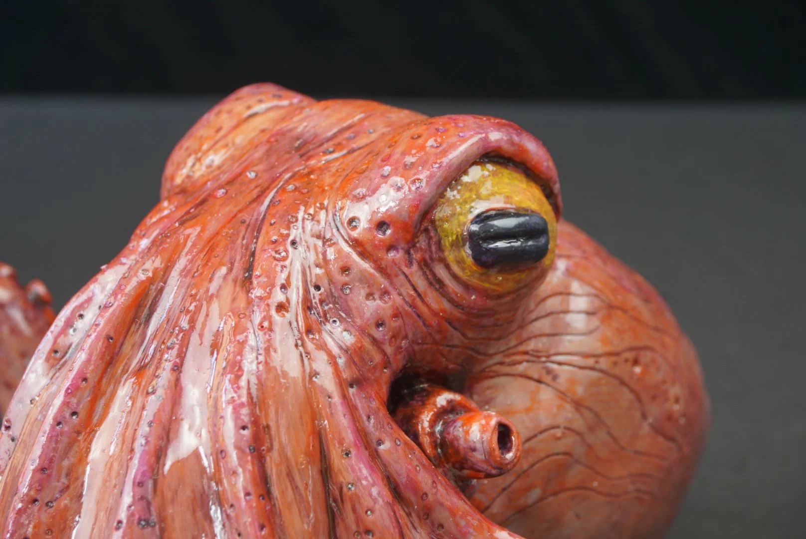 Close-up of a ceramic or sculpture model of a colorful squid with detailed features and a black eye, against a plain background.