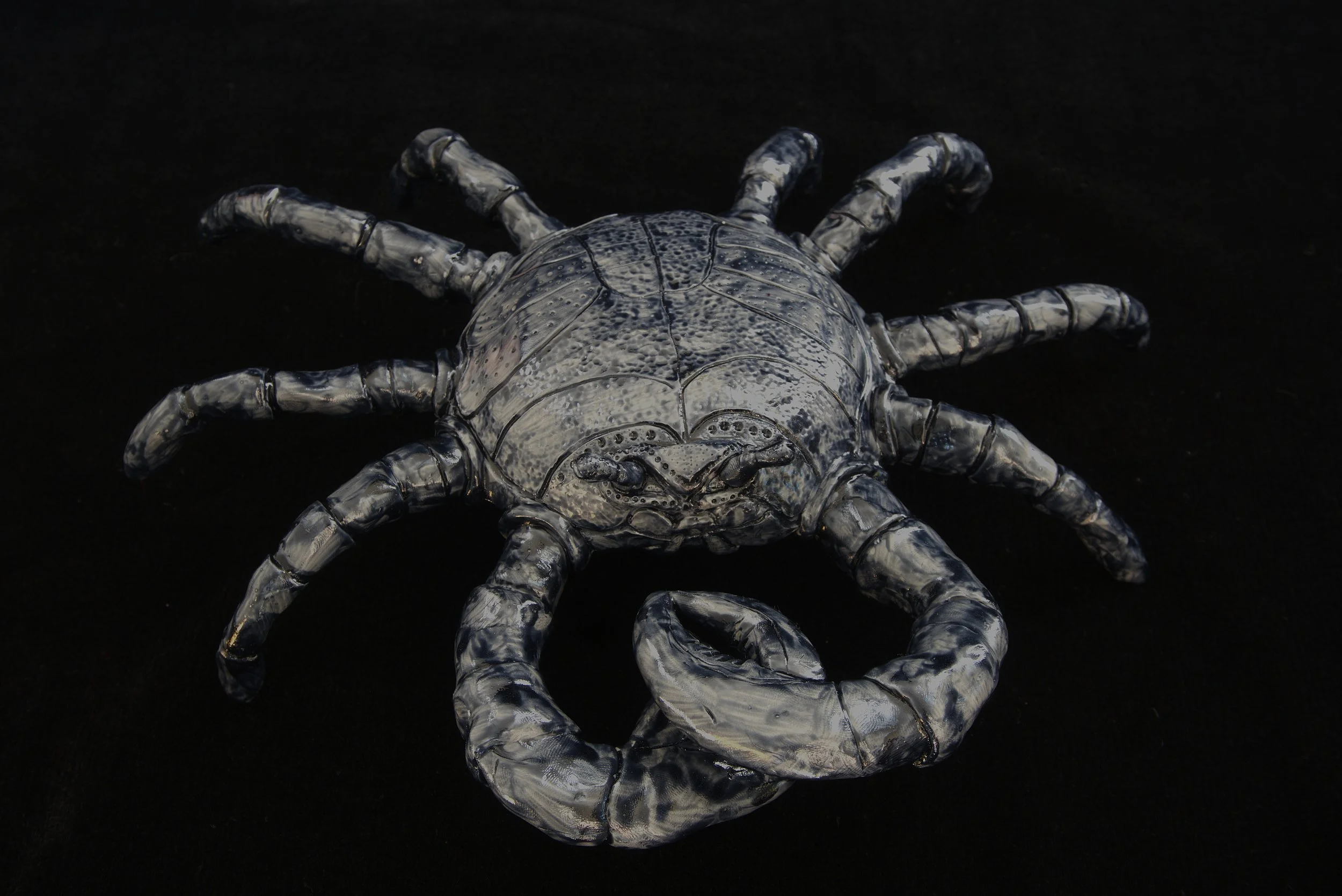 A metallic crab sculpture with detailed legs and claws, placed on a black background.