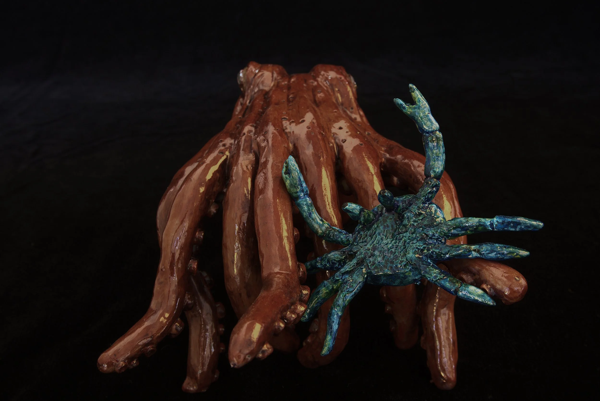 Sculpture of a large octopus with a brown, textured body and colorful blue and green arms, set against a black background.