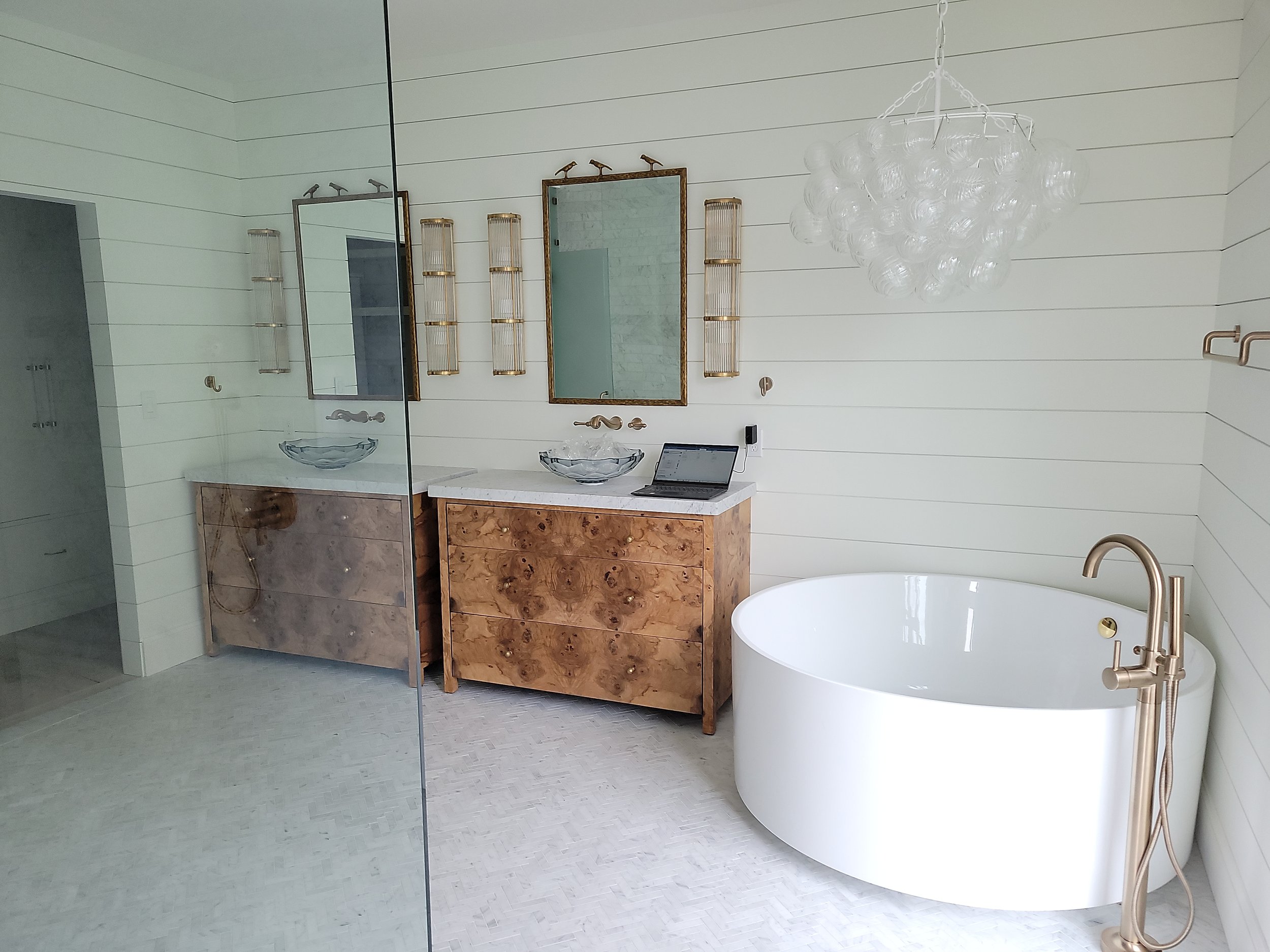 Modern bathroom with a freestanding bathtub, a wooden vanity with a glass vessel sink, large mirrors, minimalist lighting, and a chandelier made of glass bubbles.