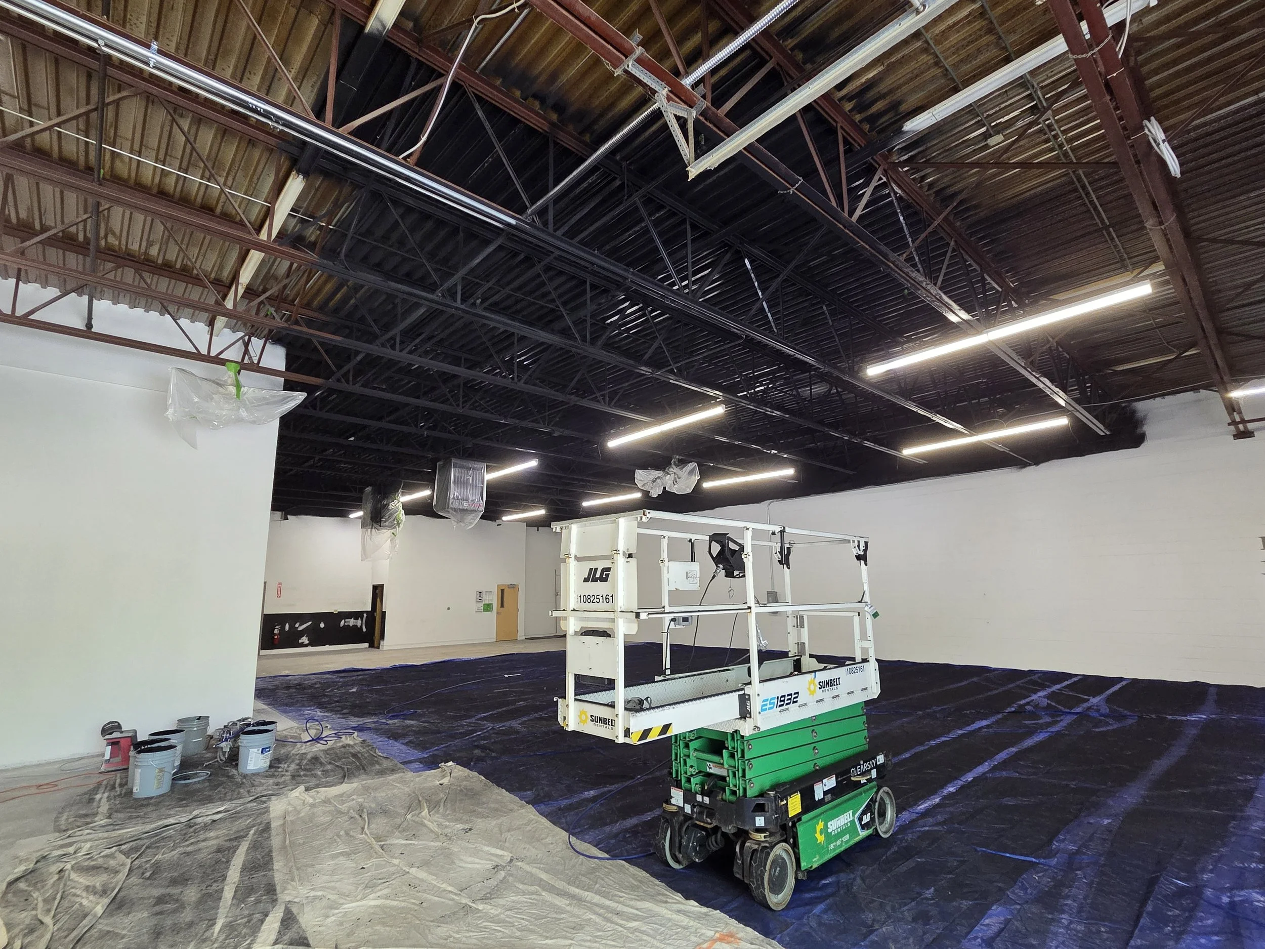 Construction or renovation site inside a building with a scissor lift, overhead lighting, and construction materials on the floor.