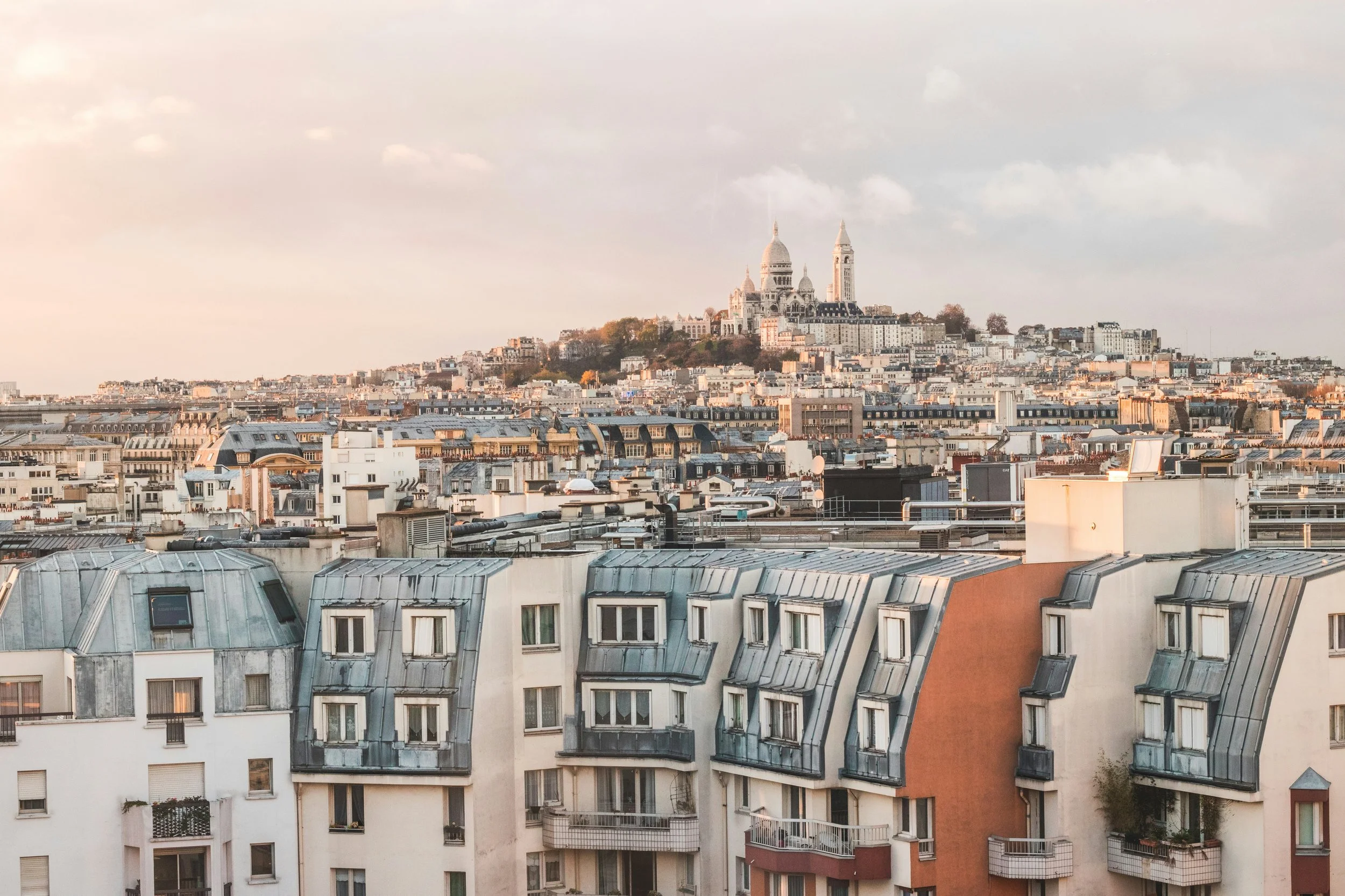 View of Paris cityscape with rooftops and Sacré-Cœur Basilica on Montmartre hill in the distance.