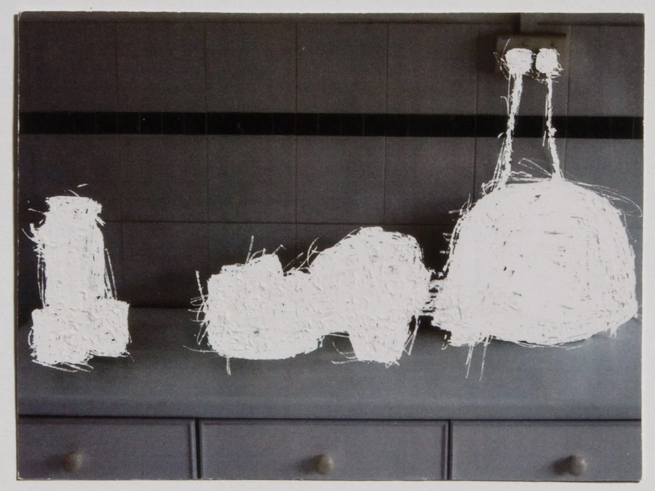 A darkened kitchen countertop with stark white silhouettes where a water bottle, a rice cooker and other household items used to be.