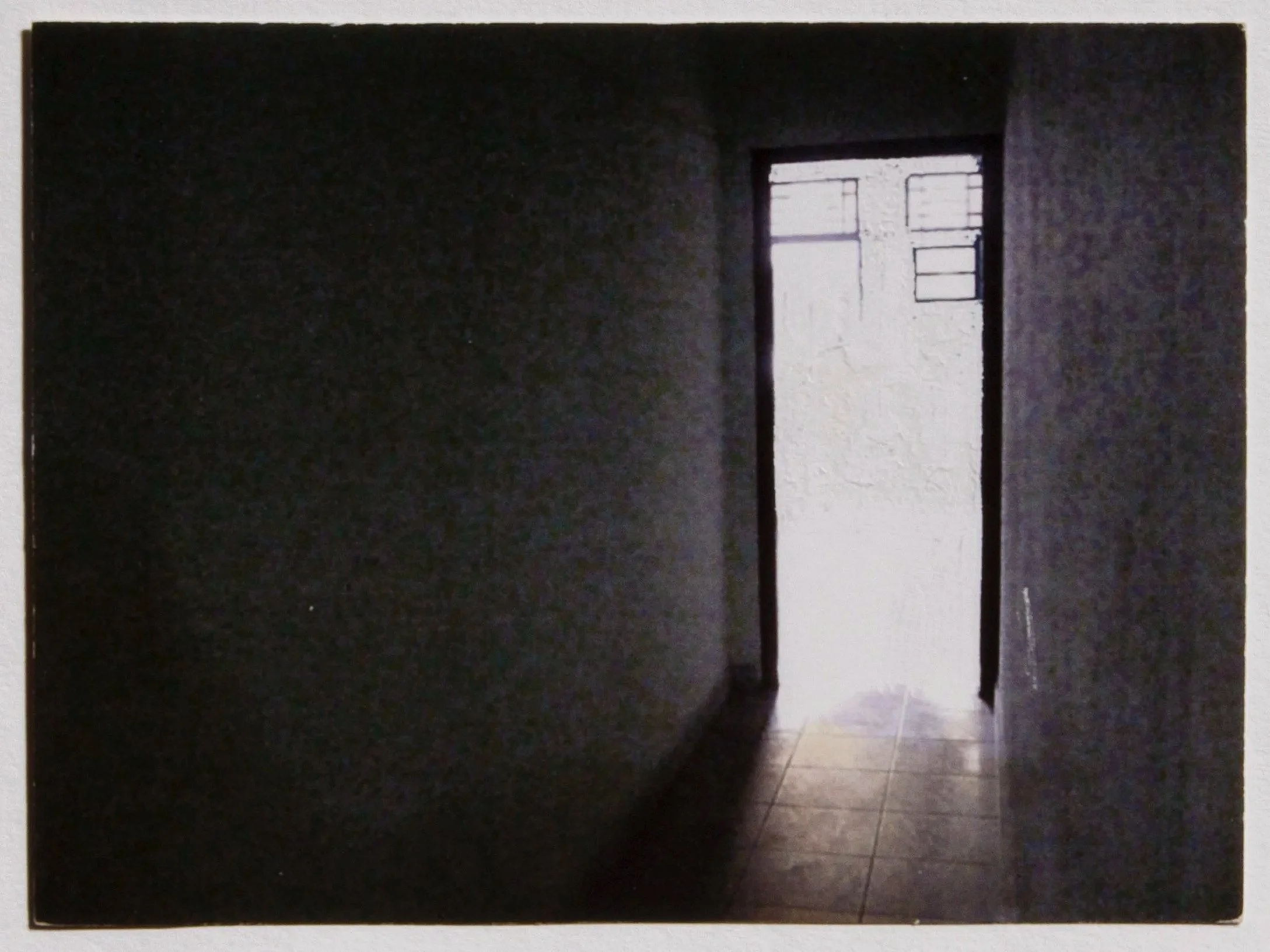 A ghostly image of an interior space featuring a narrow and dark corridor opening into a room with blinding light.