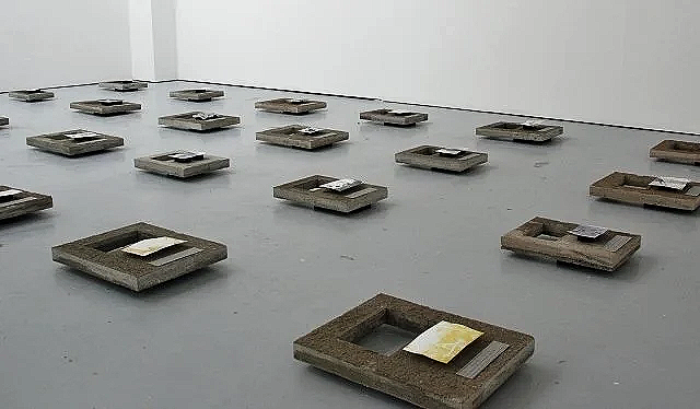 Zoomed out overview of an art installation showcasing photo prints on uniquely made concrete slabs that are rectangular with a hole in them.