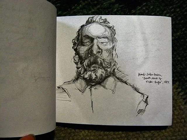 Somber black and white graphite pencil sketch in a small artist sketchbook of Victor Hugo's death mask.