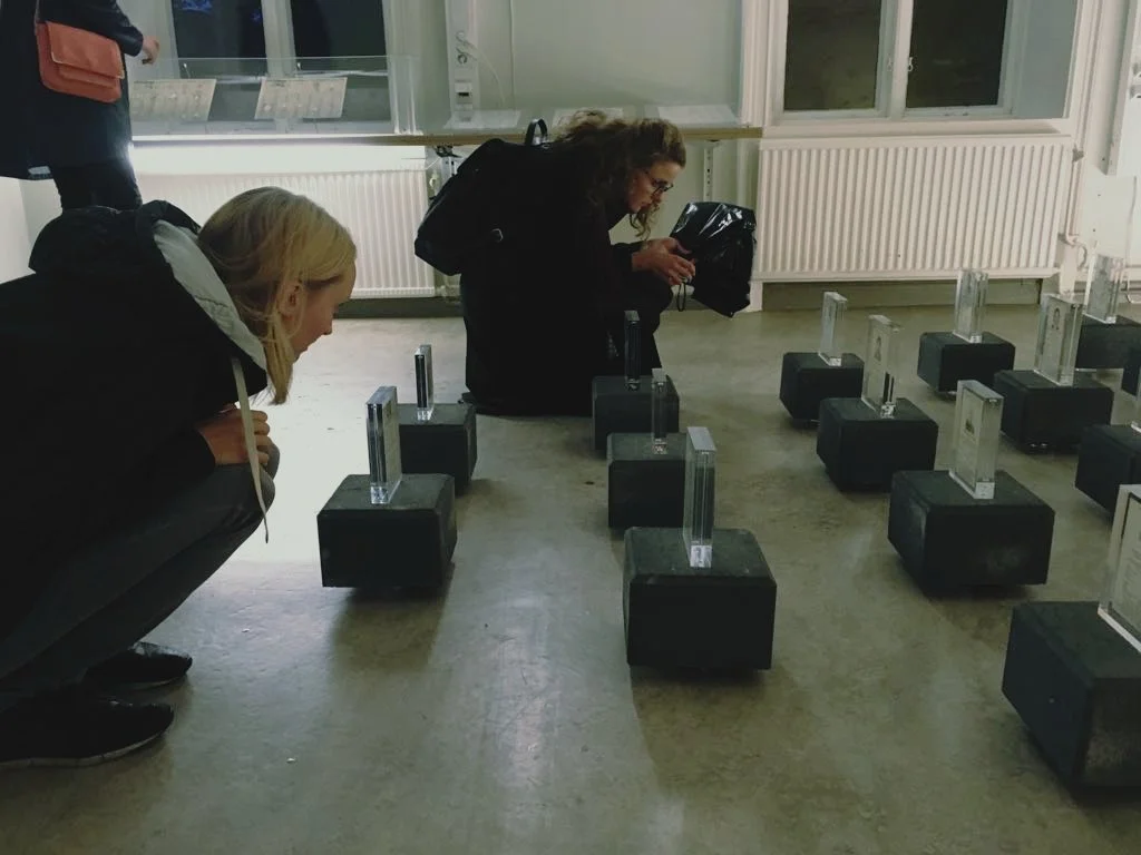 Two female visitors to the exhibition crouching down to get a closer look at the floor installation with obituaries.