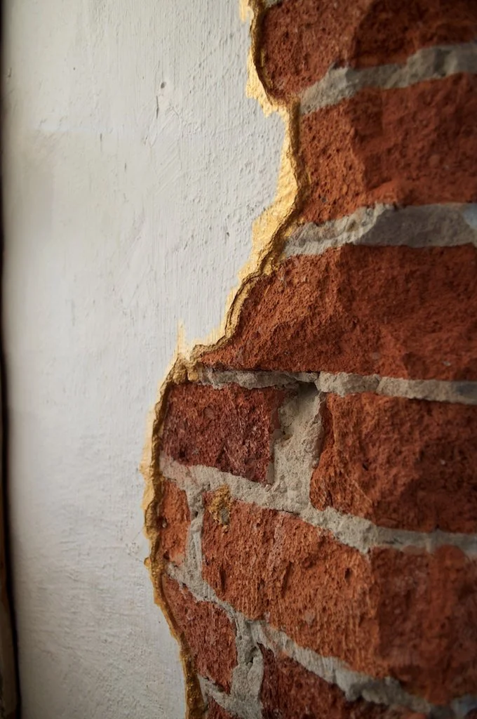 Cracked red brick wall laced with gold enamel paint.